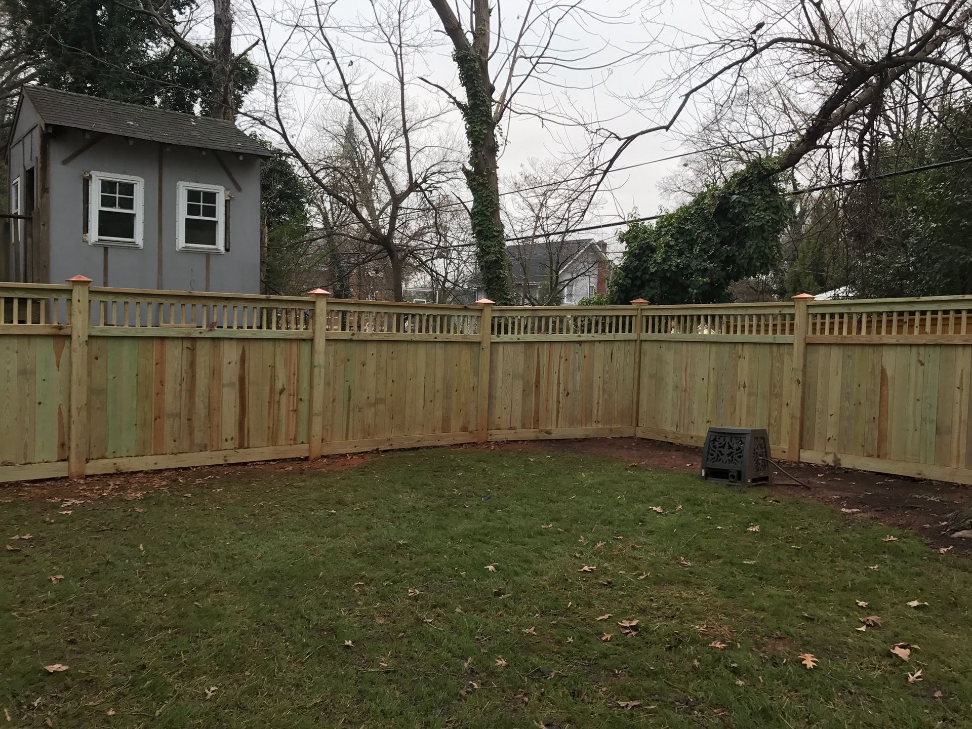 A wooden fence surrounds a lush green yard with a shed in the background.