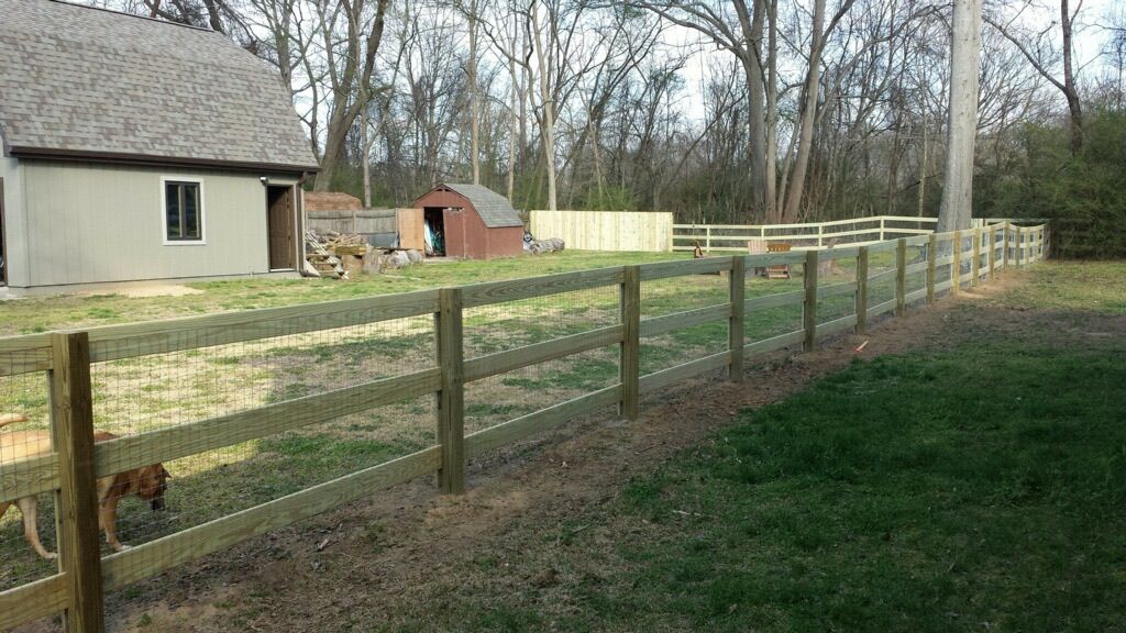A wooden fence surrounds a grassy yard in front of a house.