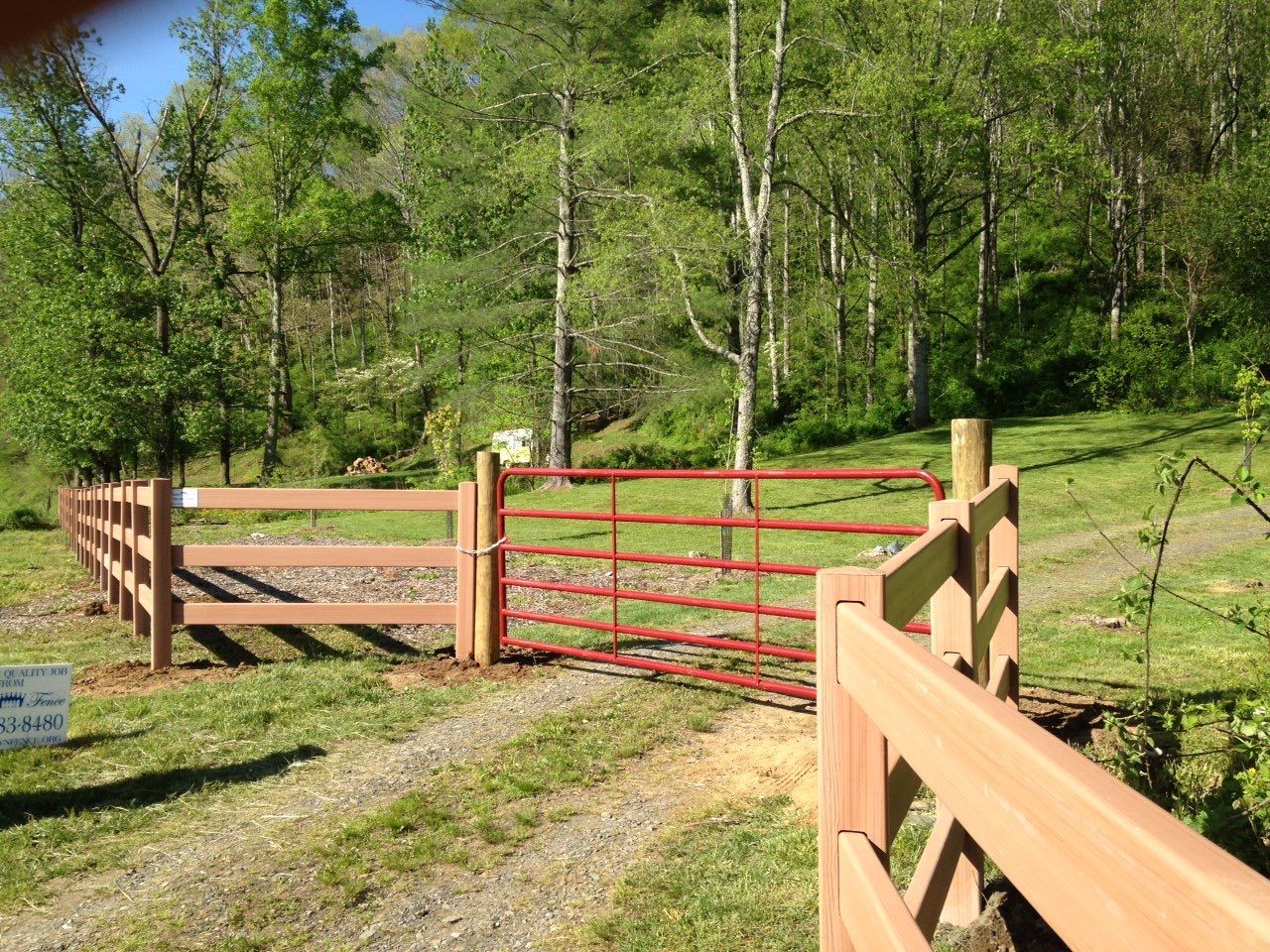 A wooden fence with a red gate in the middle of a field.