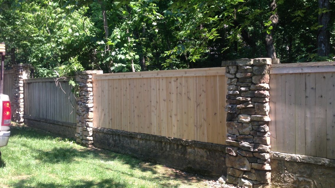 A wooden fence is surrounded by stone pillars and trees.