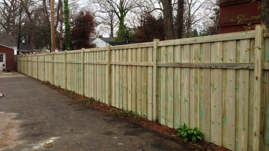 A wooden fence is sitting on the side of a road next to a house.