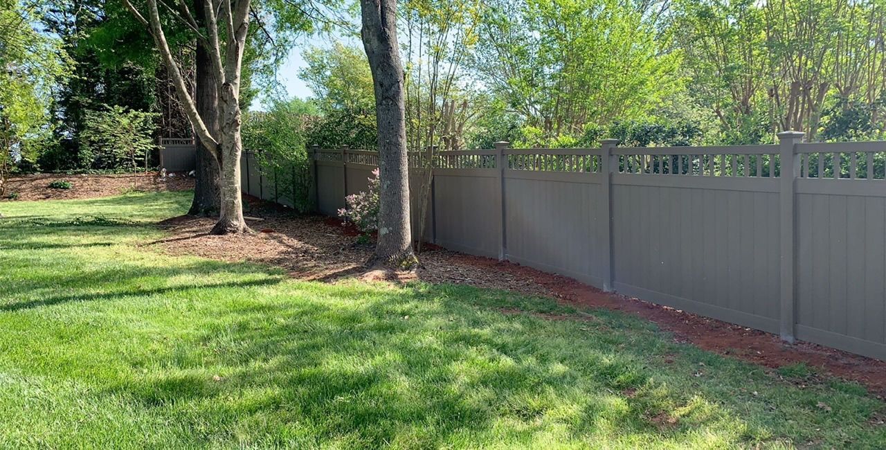 A fence surrounds a lush green yard with trees in the background.