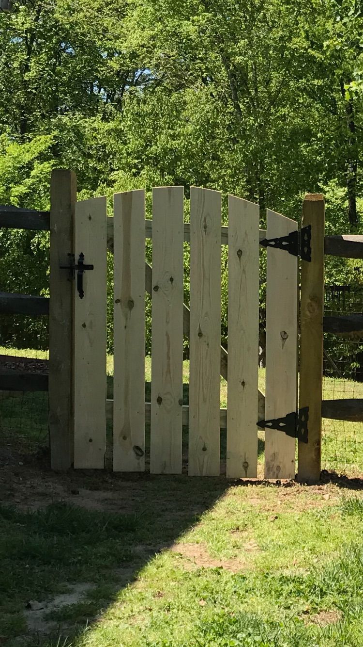 A wooden gate is sitting in the middle of a grassy field next to a wooden fence.