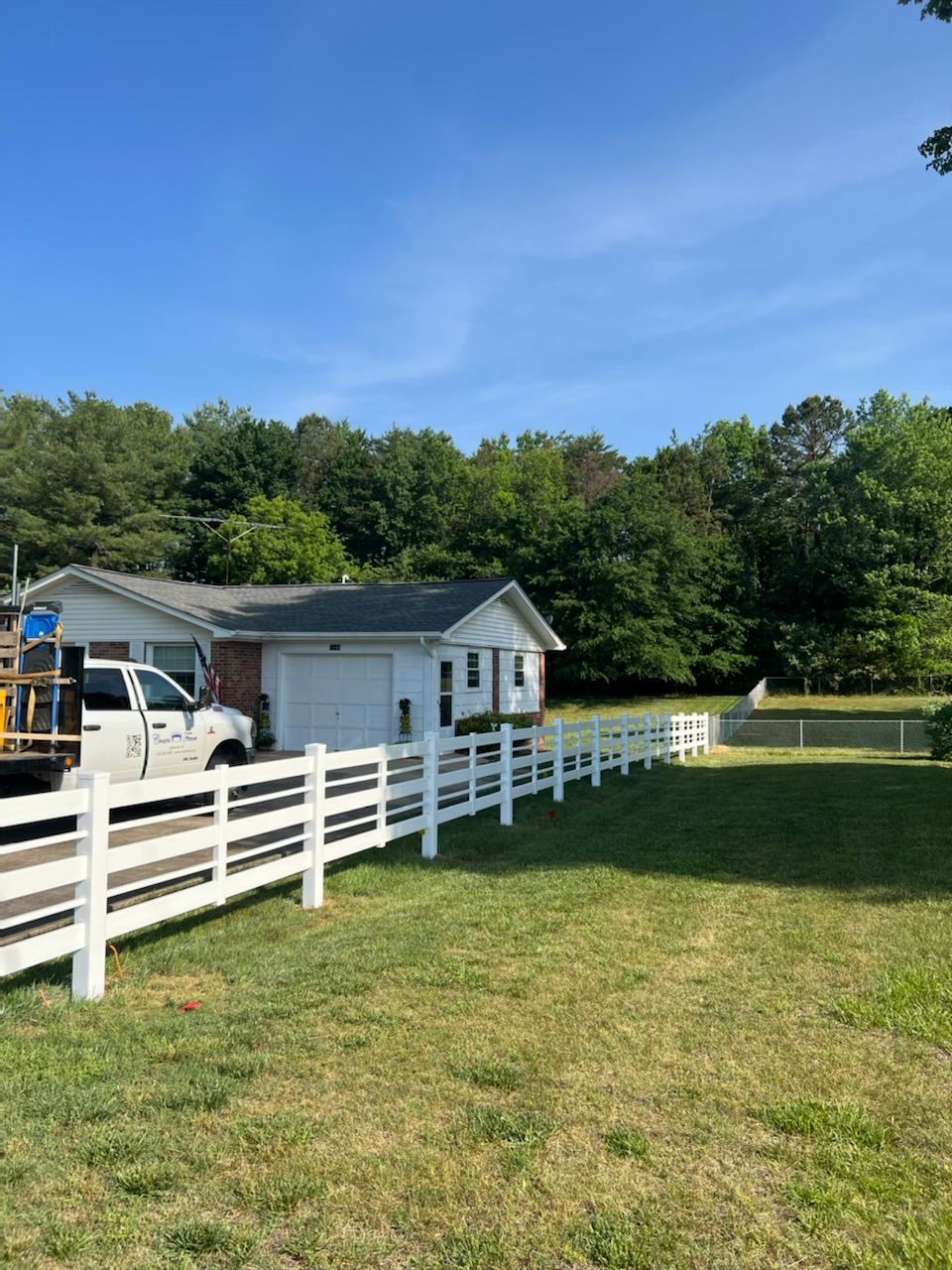 A white truck is parked in front of a house with a white fence.