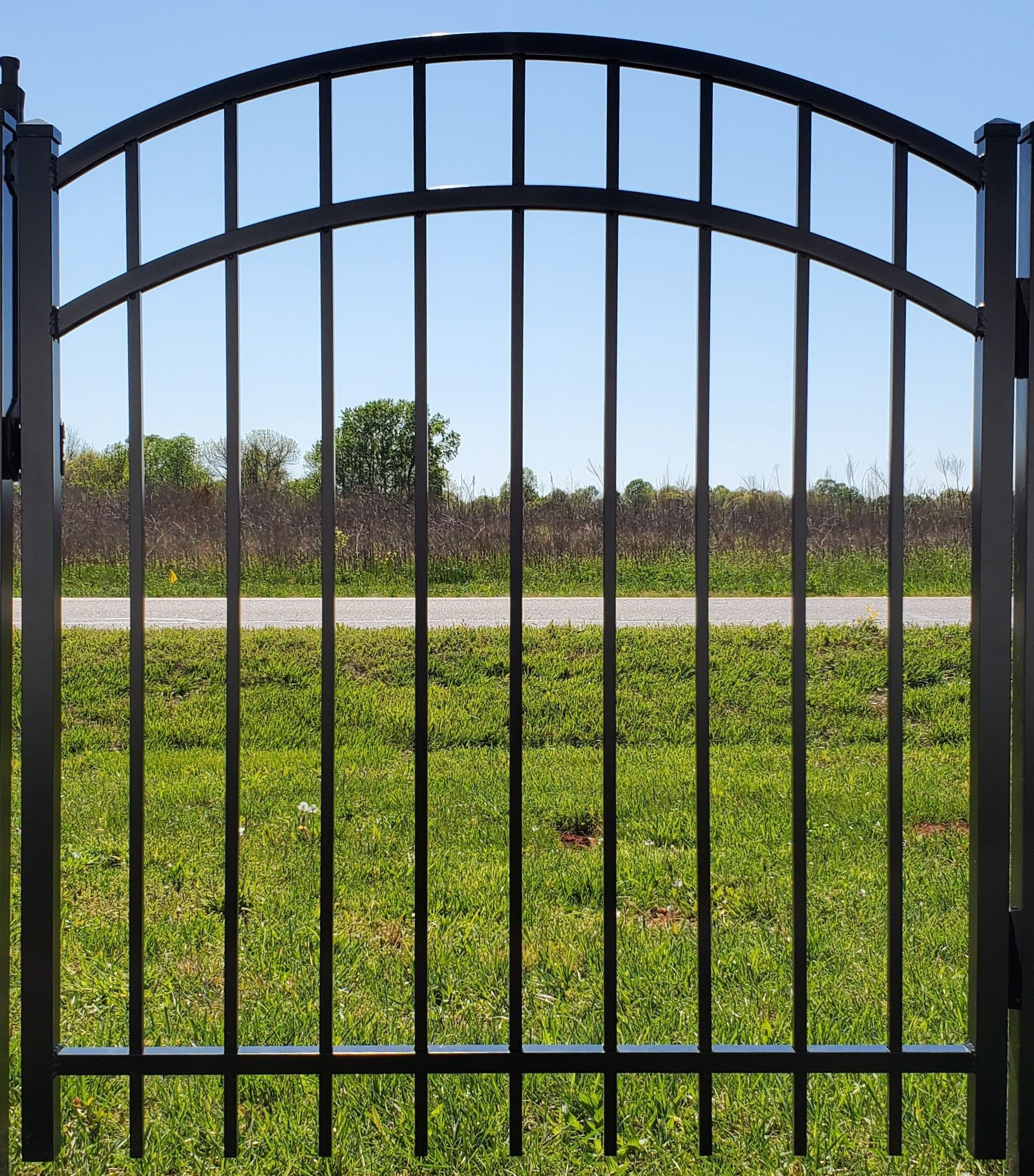 A black wrought iron gate is open to a grassy field.