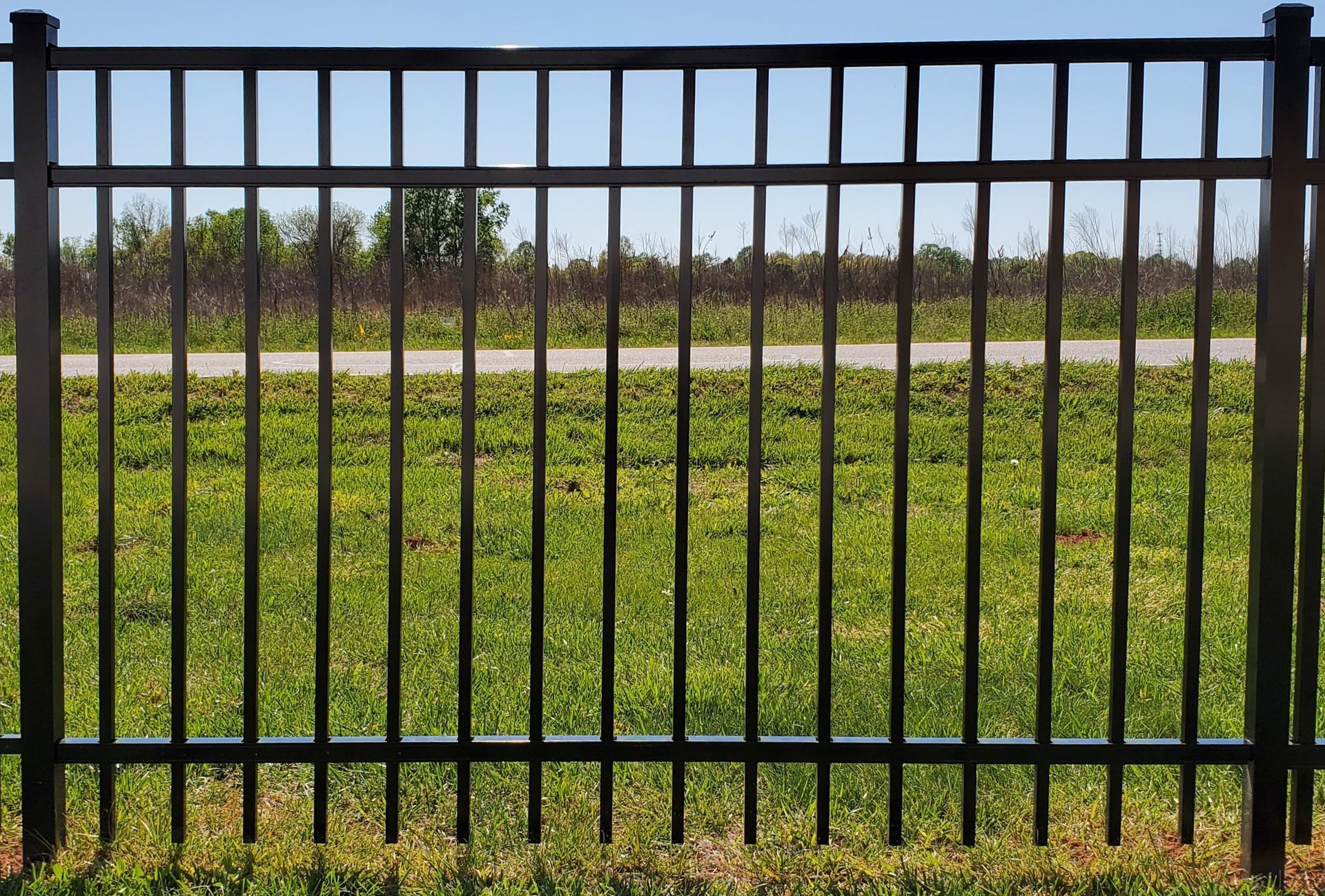A black metal fence surrounds a lush green field.