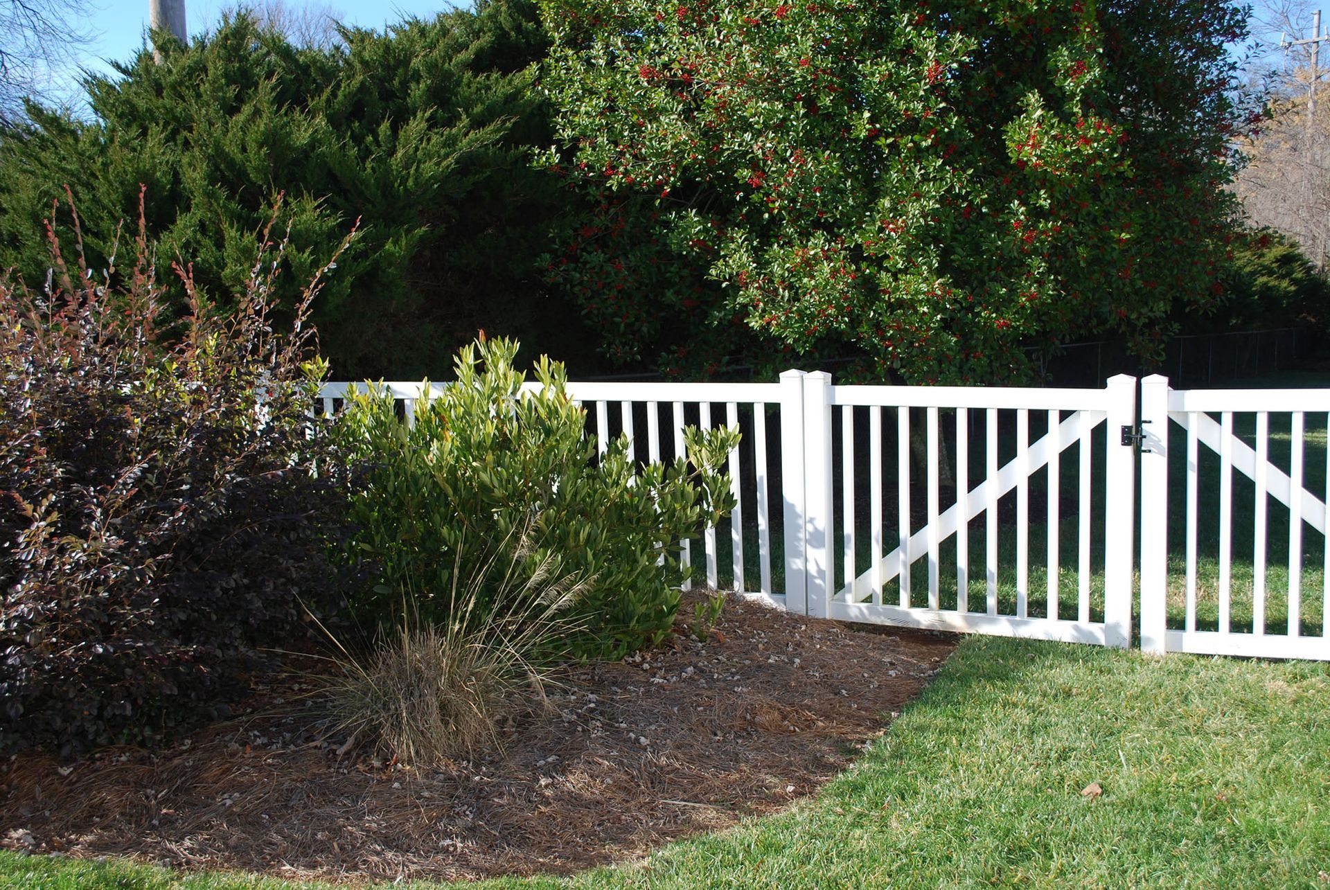A white fence with a gate is surrounded by trees and bushes