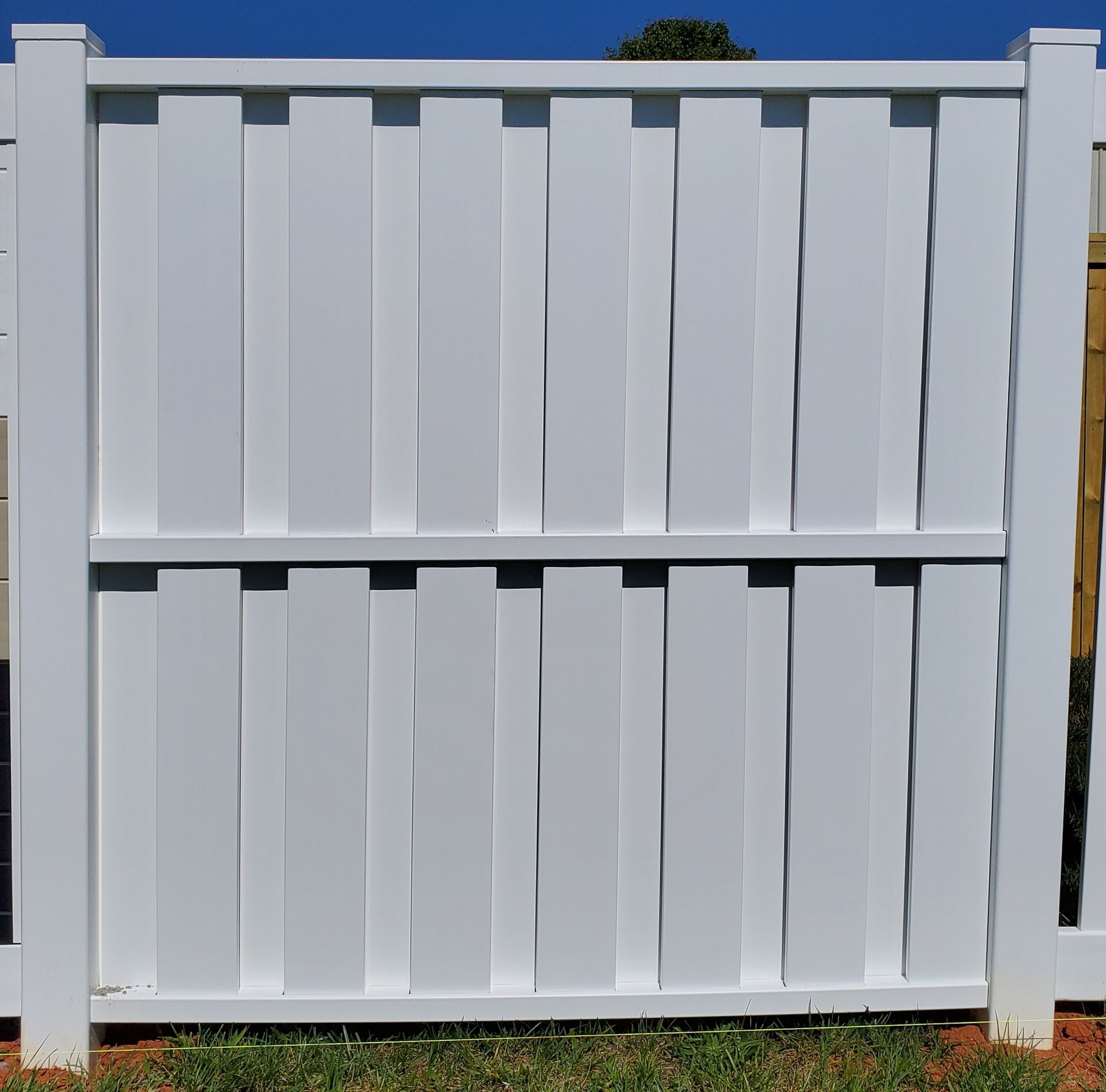 A white fence is sitting in the grass in front of a blue sky.