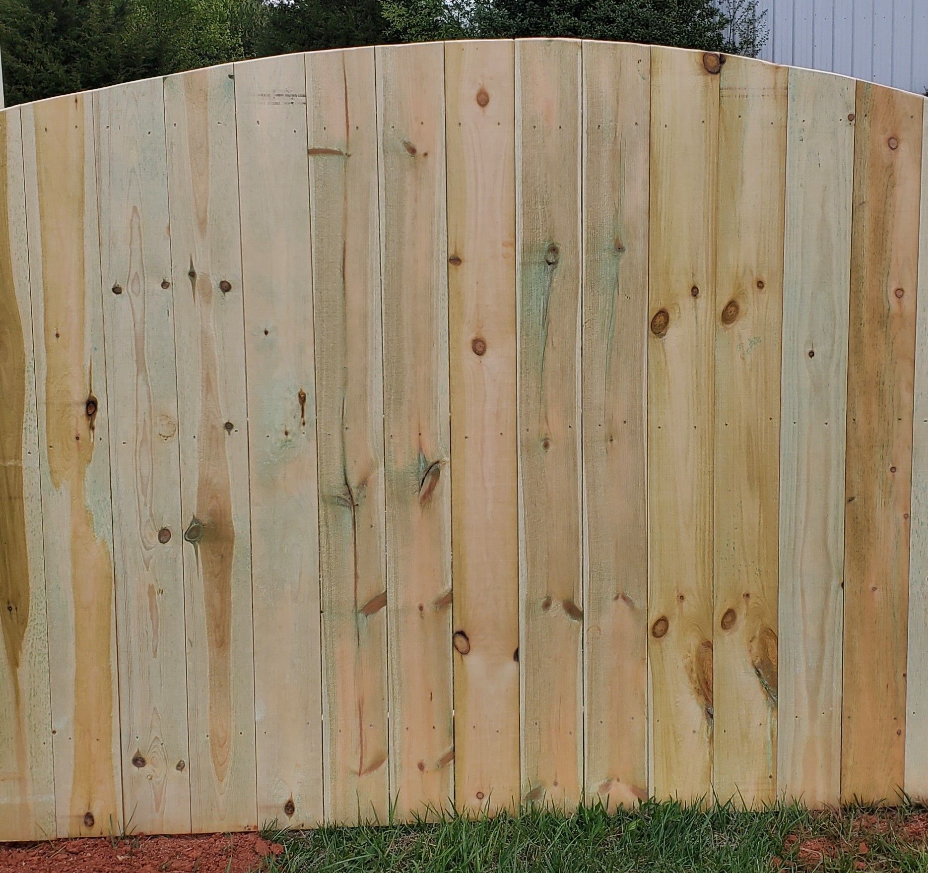 A wooden fence with a curved top sits in the grass
