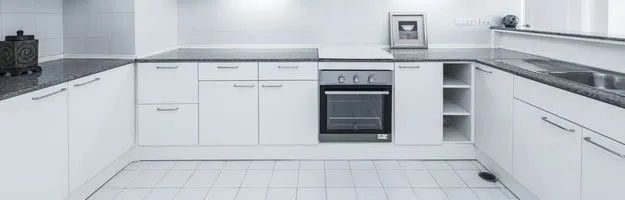White kitchen with modern cabinetry and built-in oven. Tiles on the floor and countertop.
