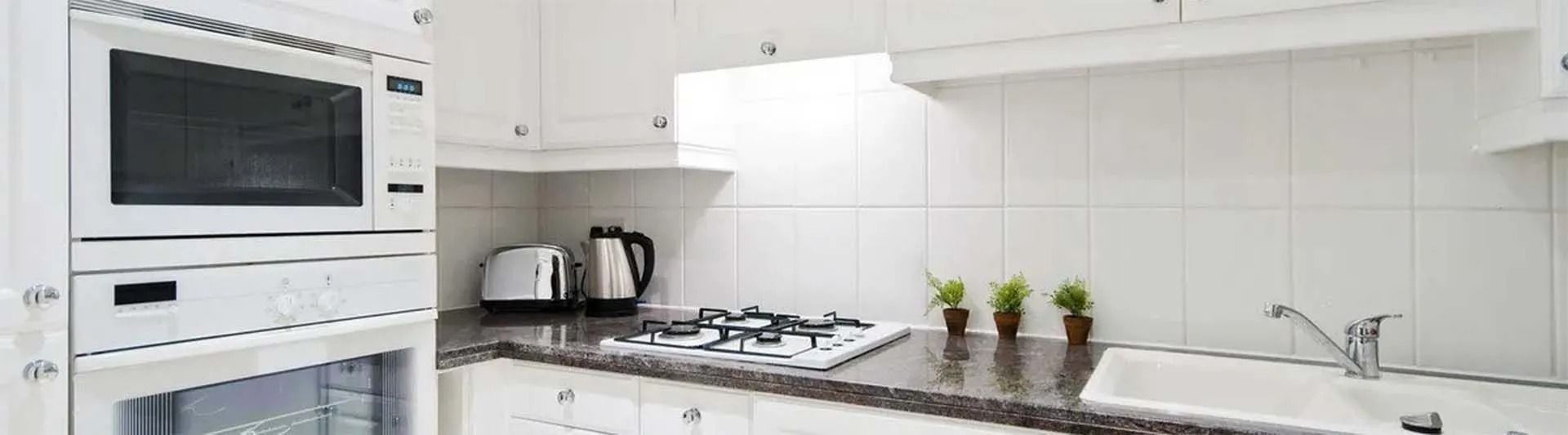 A modern white kitchen with a built-in microwave, stove, and countertop appliances.