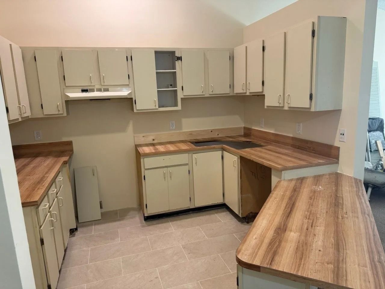 Cream-colored kitchen cabinets with wooden countertops. The room has tiled flooring.