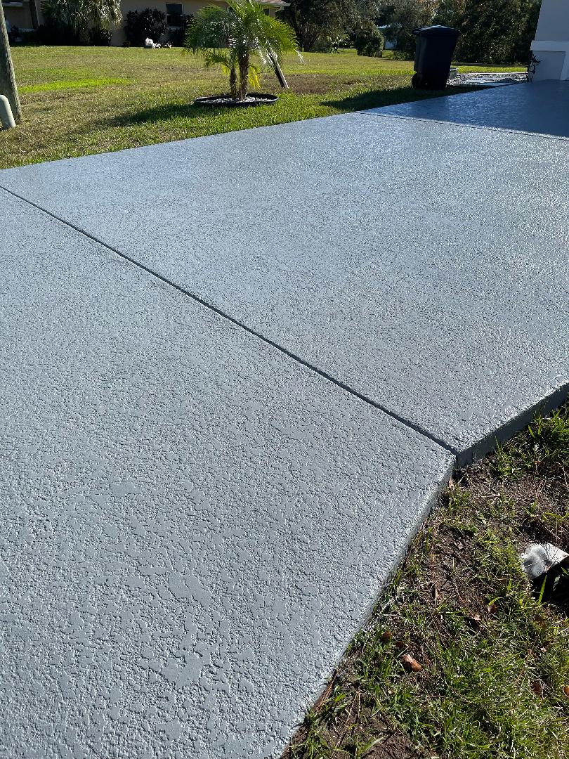 A concrete driveway with a grassy border and a tree in the background.