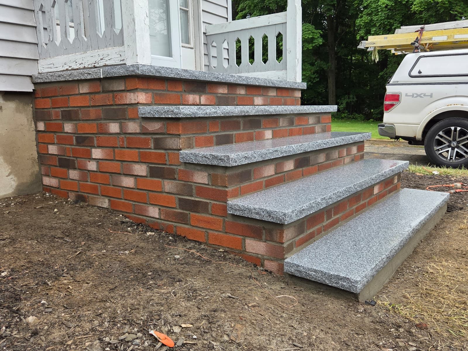 Brick front porch with three gray stone steps and a parked white SUV nearby