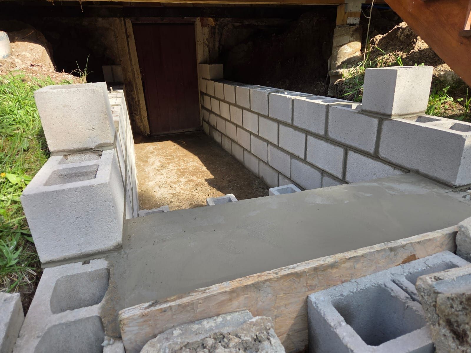 Concrete walkway beside cinder block retaining wall leading under a dark underpass