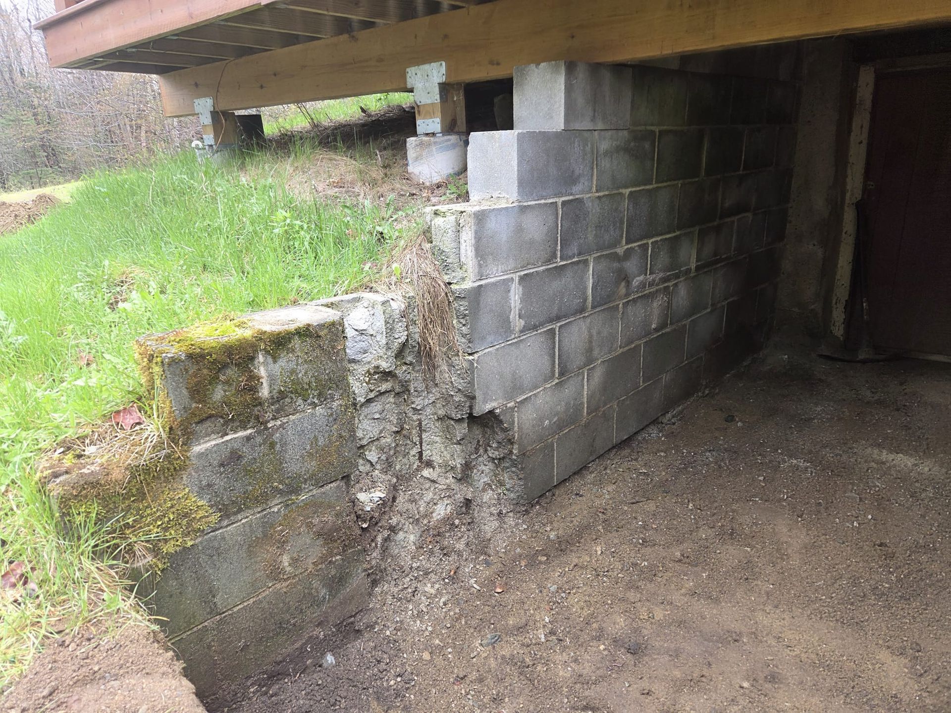 Damaged concrete block foundation under a raised deck, with crumbling corner and exposed soil beside it