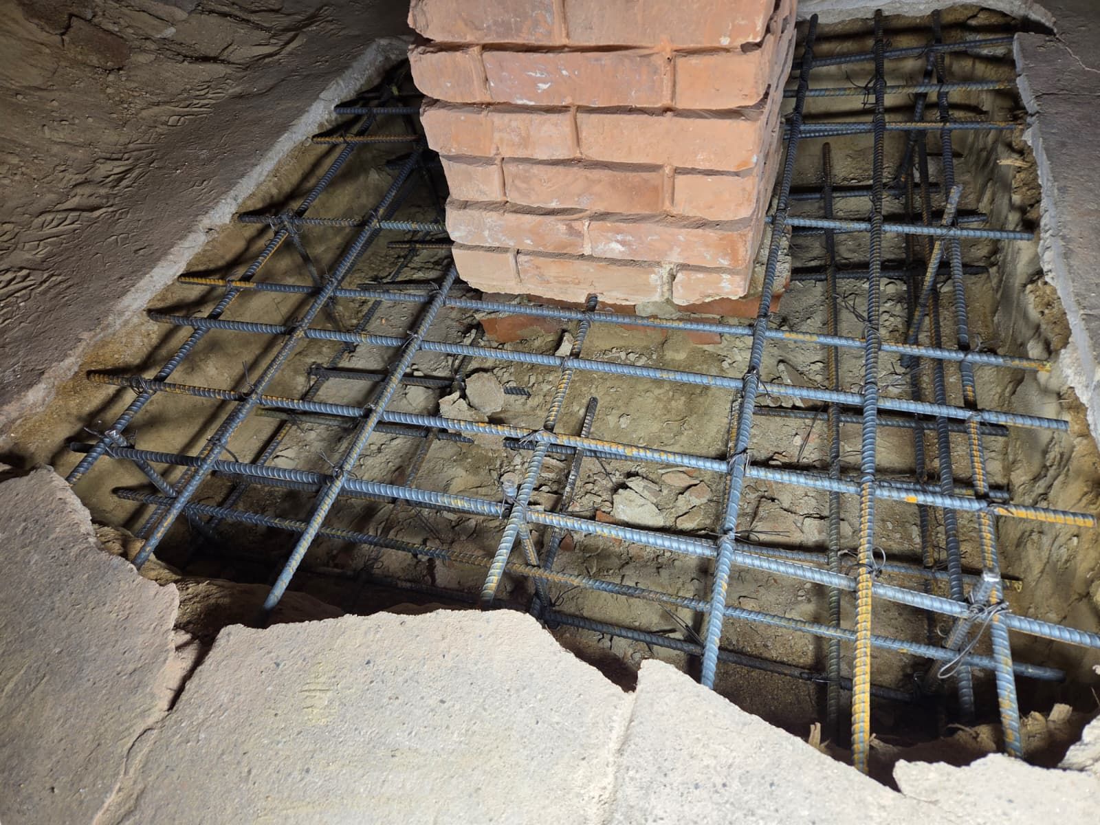 Cracked concrete floor around exposed steel rebar and a brick column base