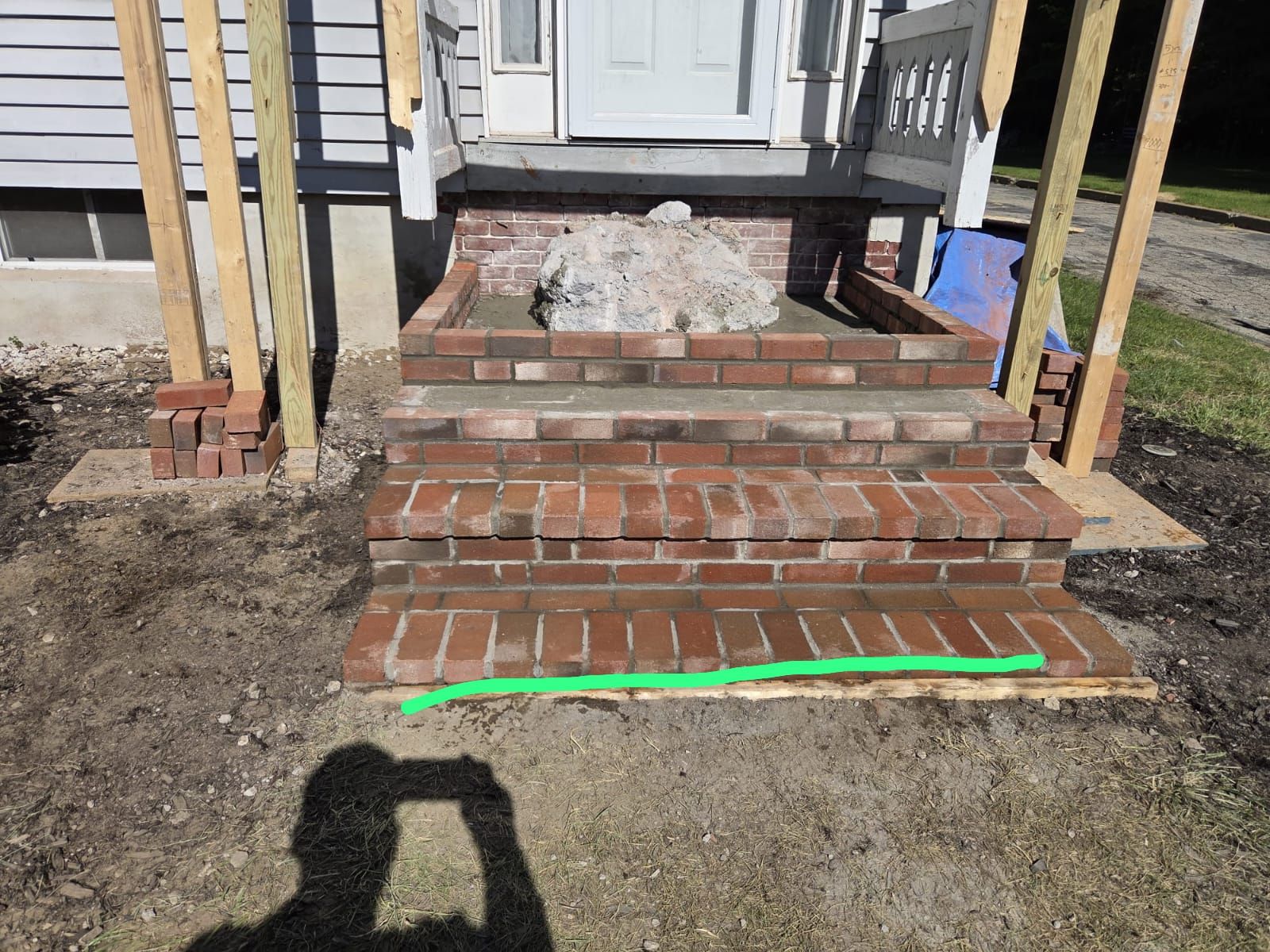 Brick front steps with a green-marked bottom edge and wooden rail posts leading to a house porch