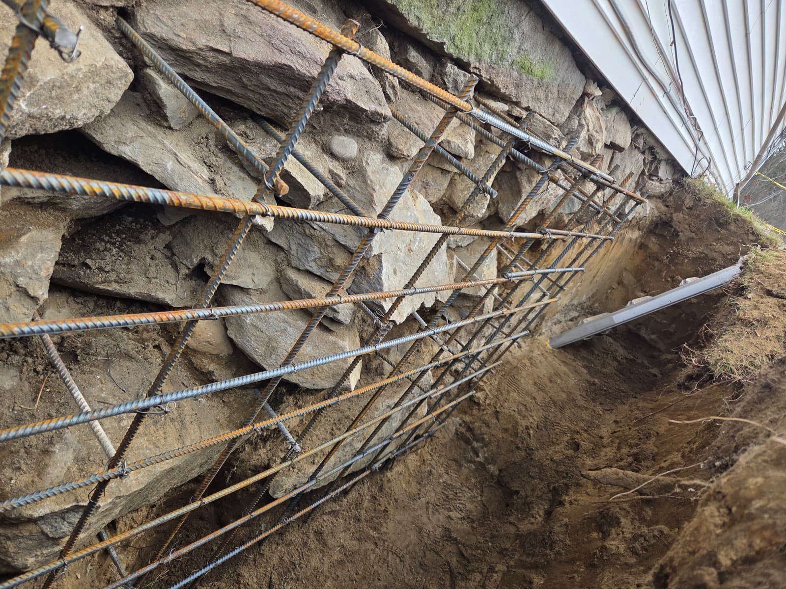 Damaged stone retaining wall with bent rebar and collapsed earth on a construction site