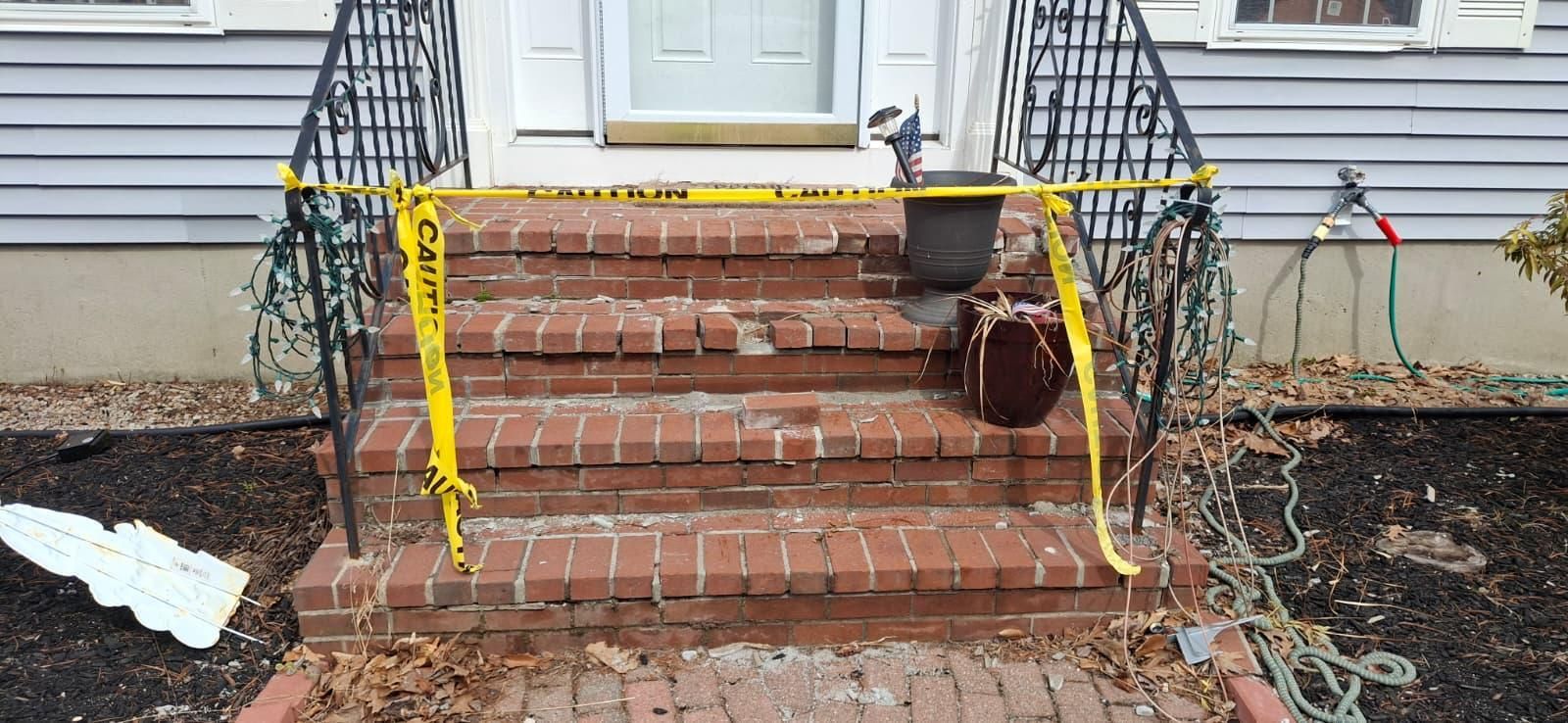 Brick front steps with yellow caution tape and a railing beside a house entrance