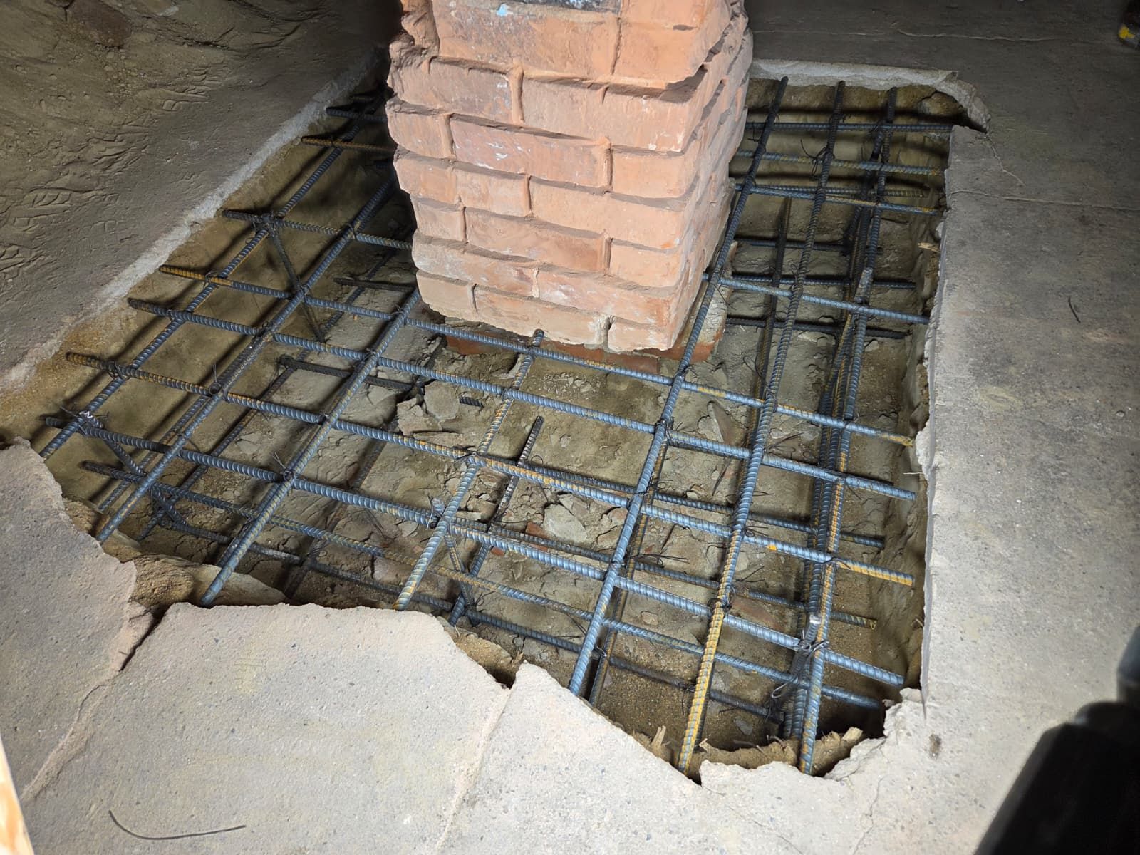 Cracked concrete floor around a brick pillar, exposing steel rebar beneath