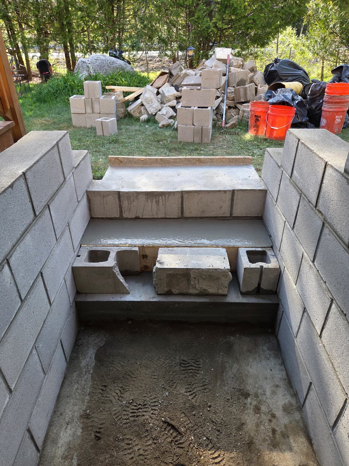 Partially built cinder block walls and concrete steps at an outdoor construction site with stacked blocks in back