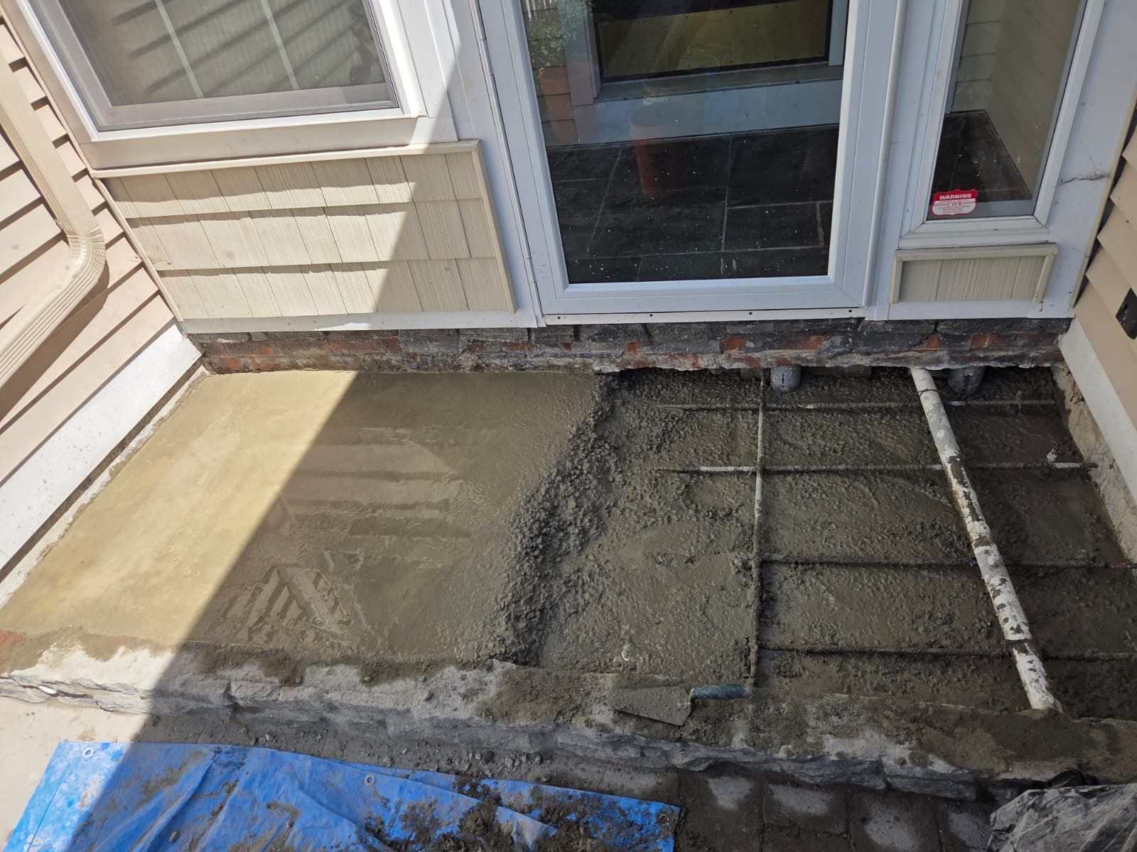 Damaged concrete patio beside sliding glass doors, with torn surface and patchy repairs