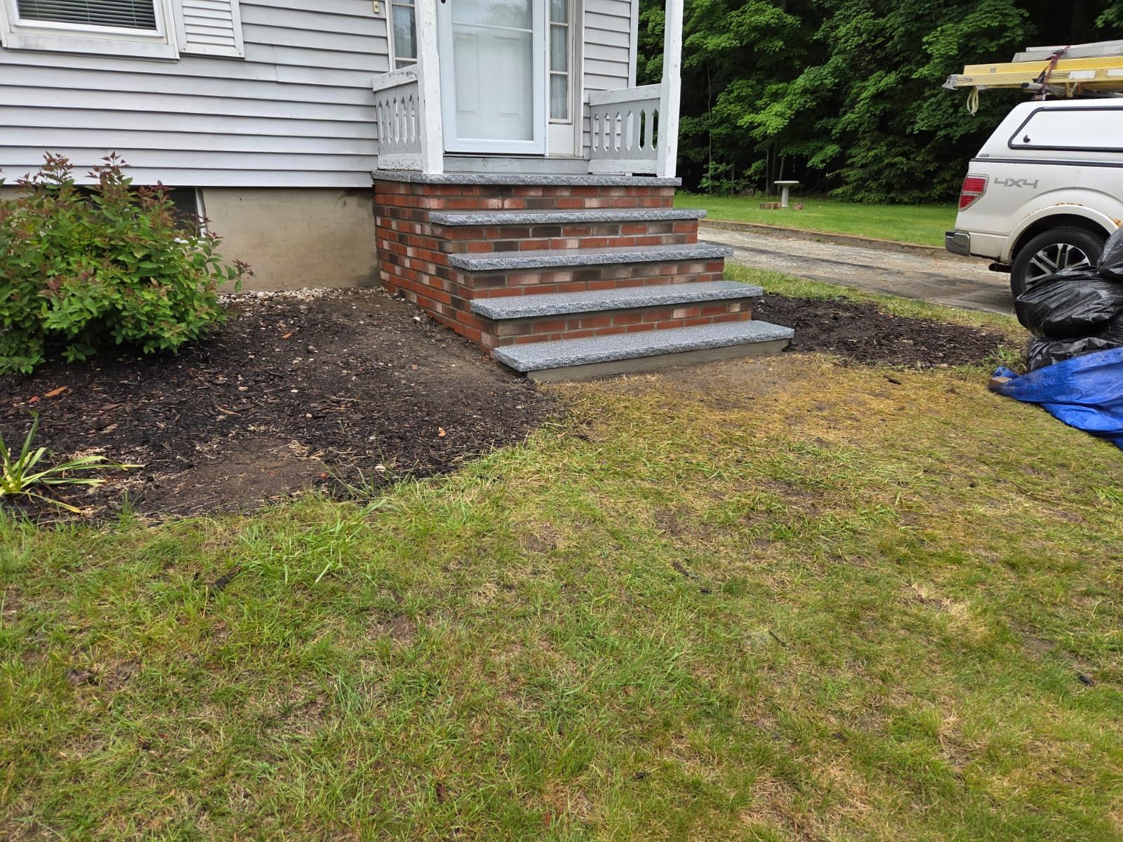 House front steps with brick sides and gray stairs beside a grassy lawn and parked SUV