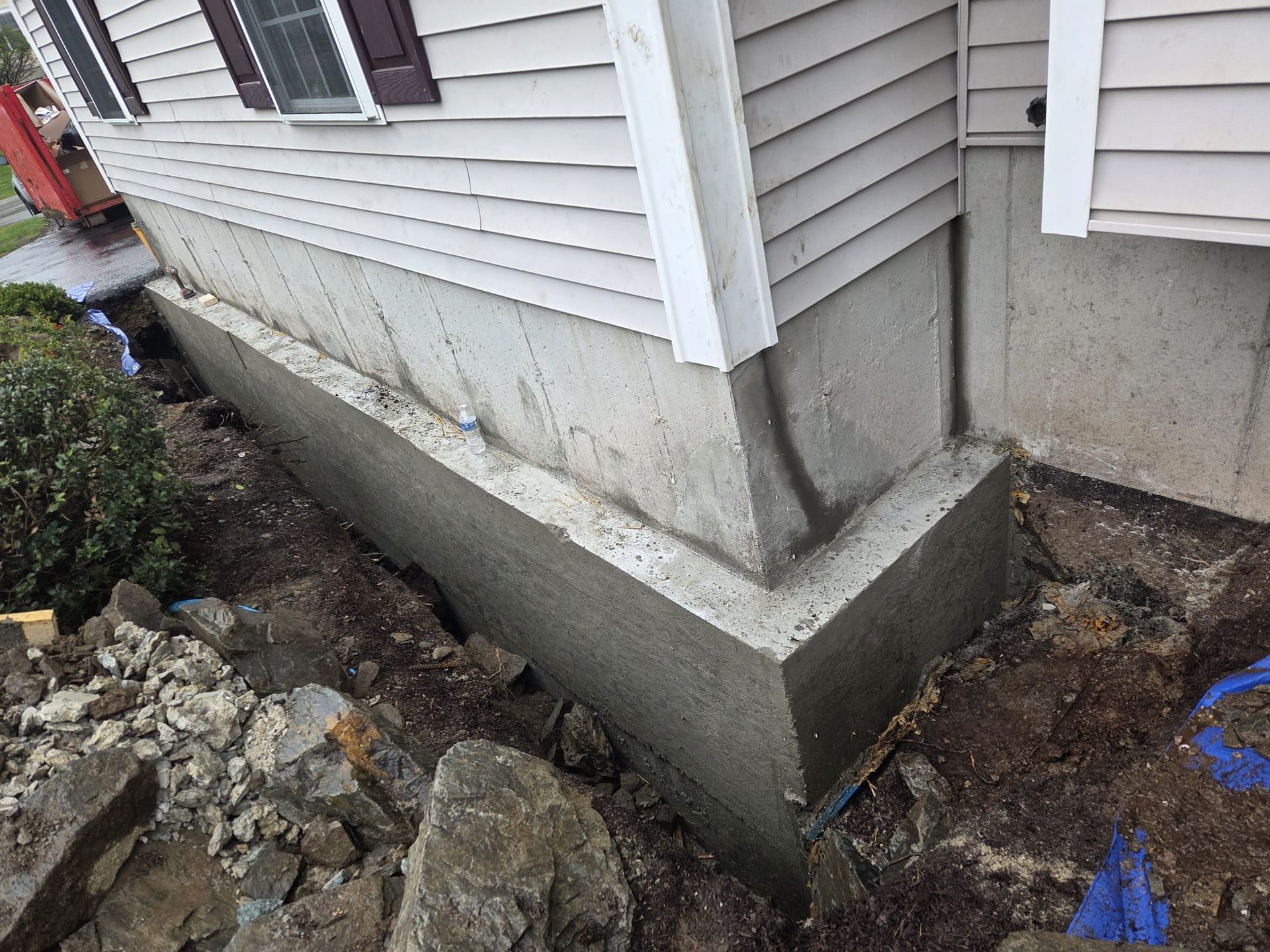 Cracked concrete foundation along house siding with exposed soil and debris near corner of home