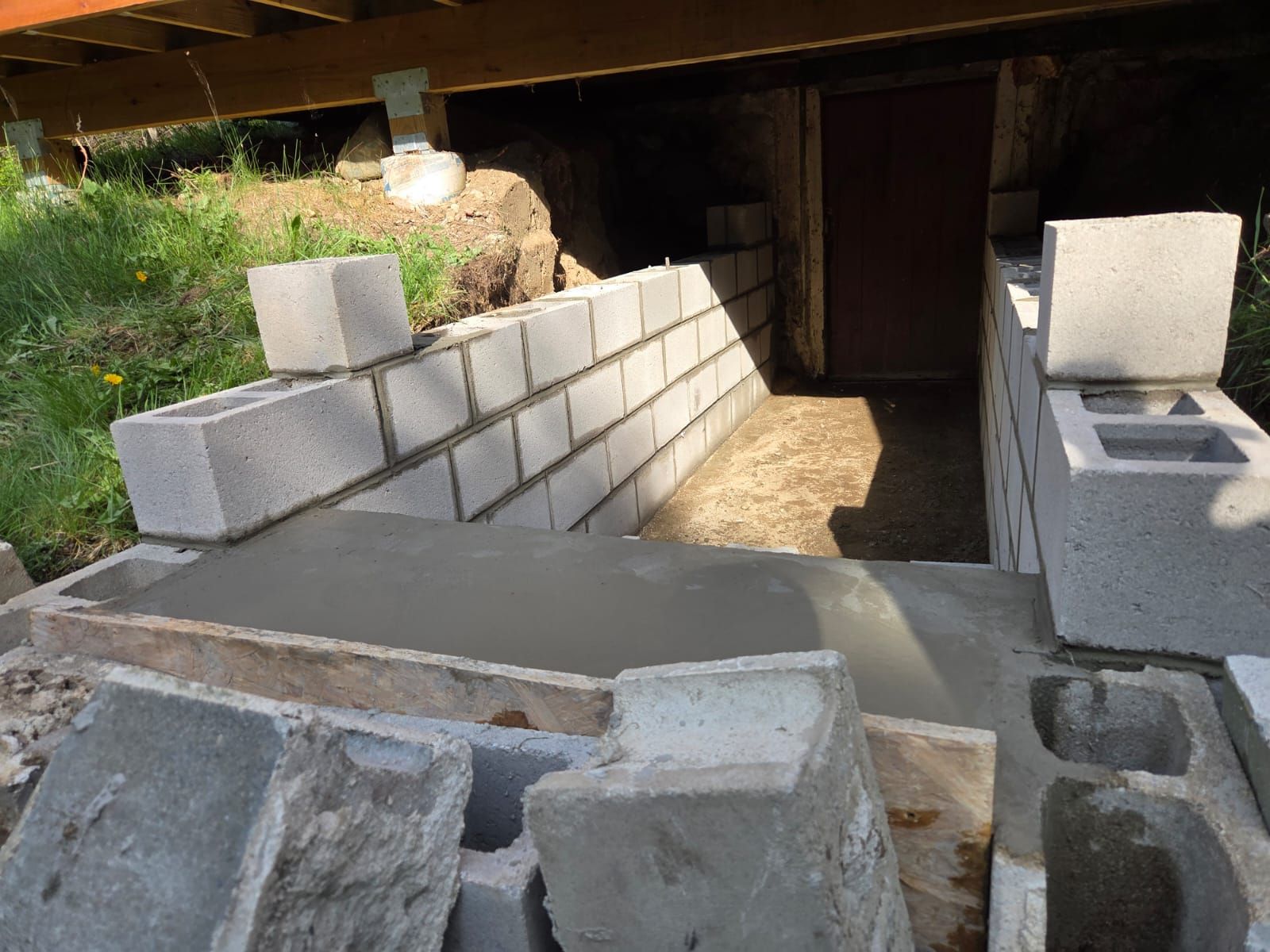 Partially built concrete ramp and retaining walls under a structure, with cinder blocks and rubble nearby
