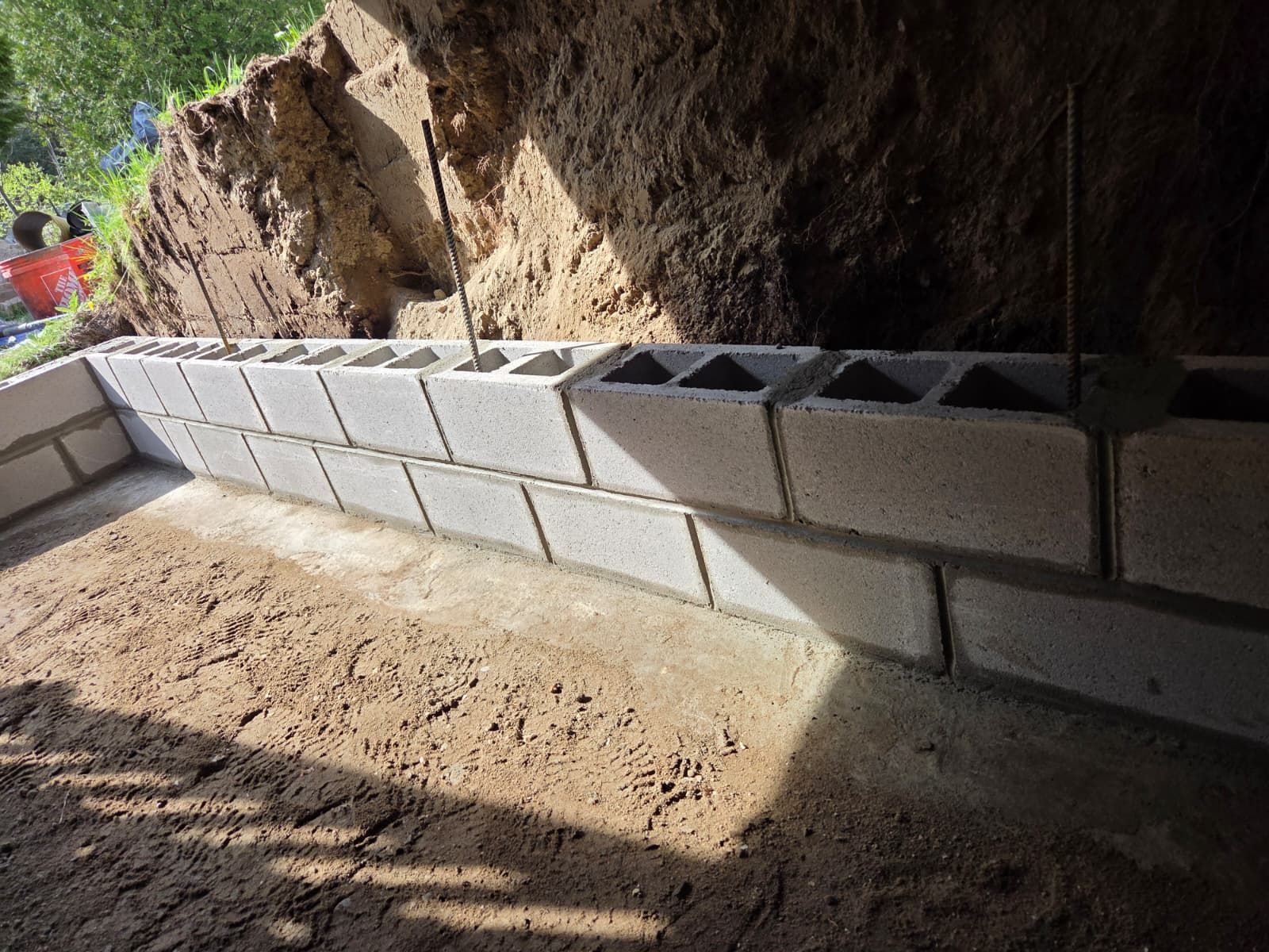 Cinder block retaining wall built against a dirt slope beside a sunlit path