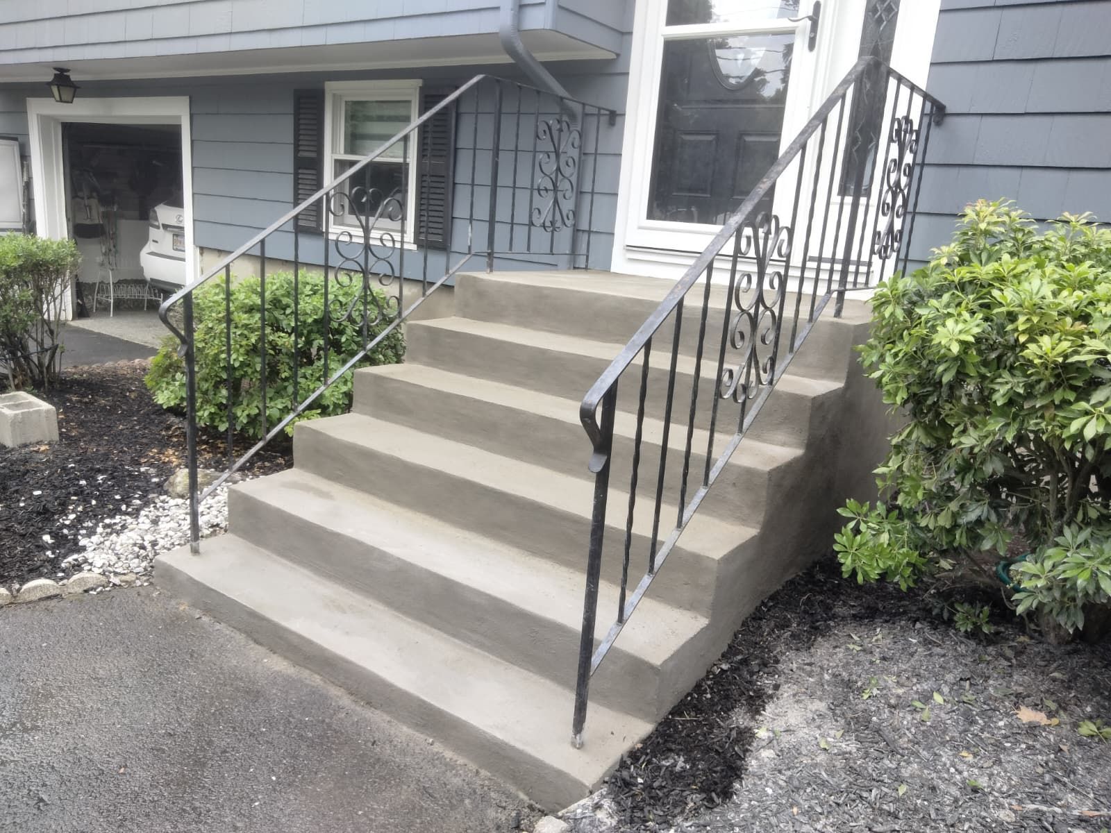 Concrete front steps with black railings leading to a gray house entrance.