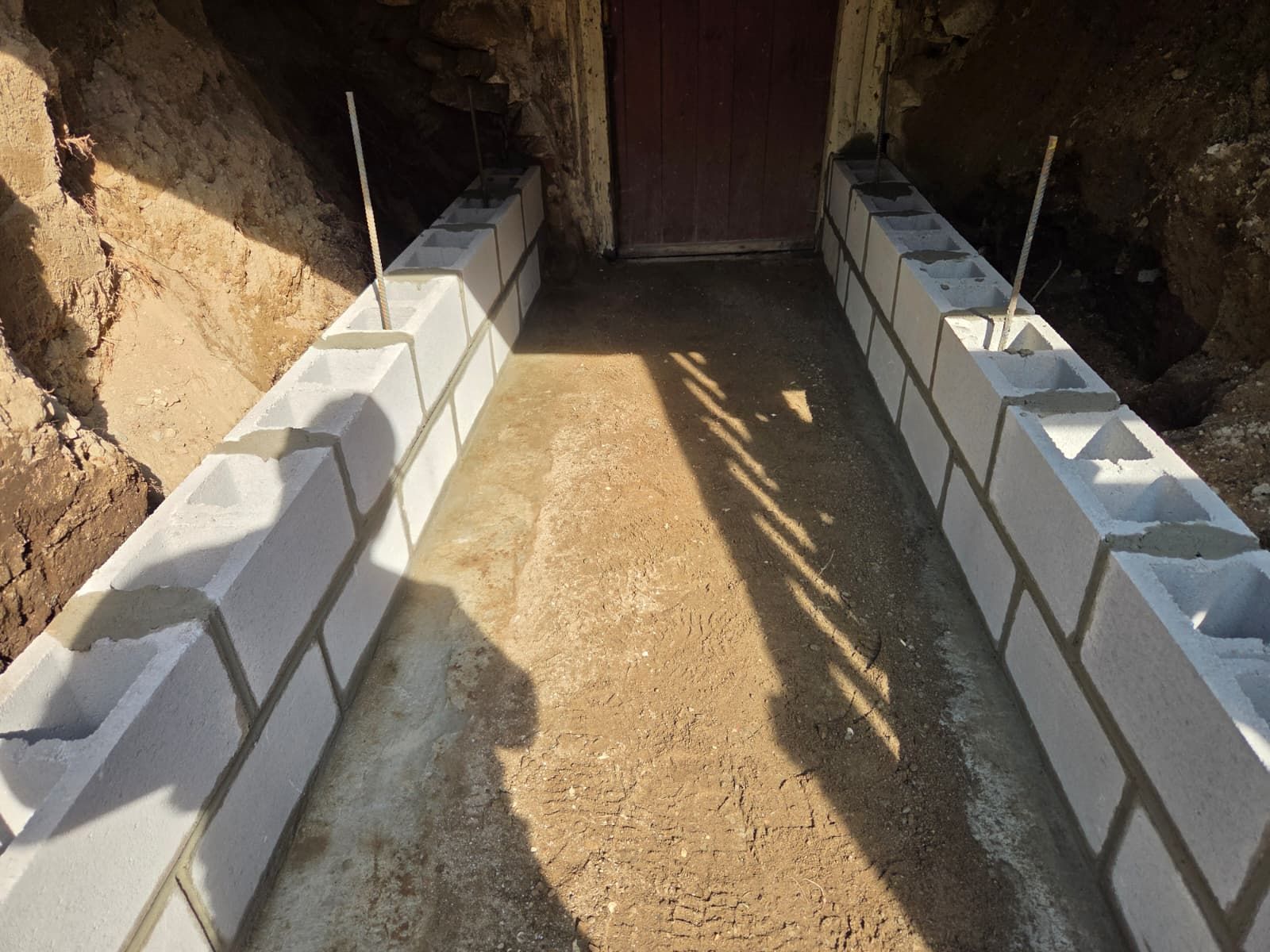 Concrete block walls forming a narrow trench leading to a wooden door in an earthen hillside