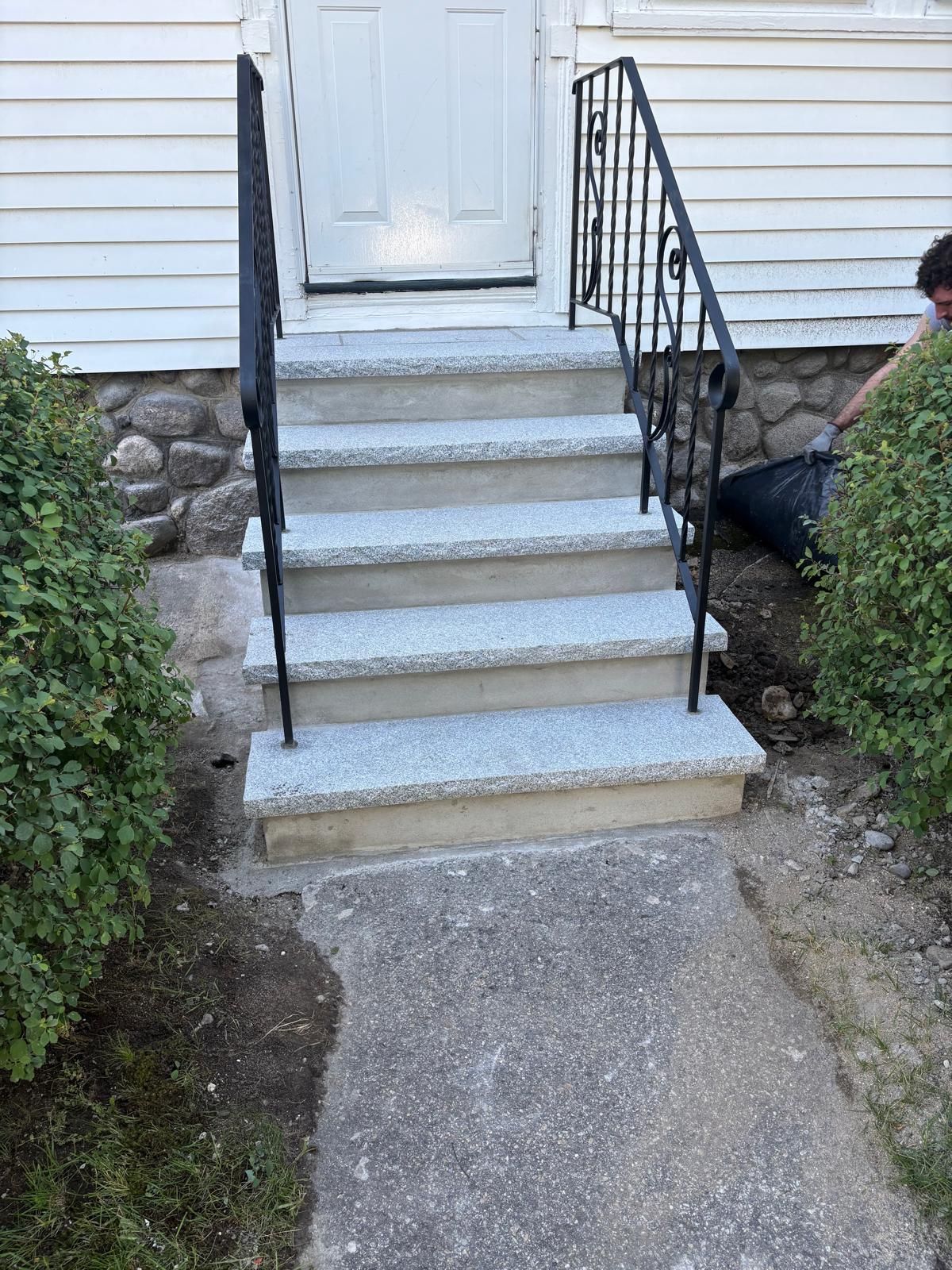 Front steps to a white house with black railings and a stone walkway leading up to the door