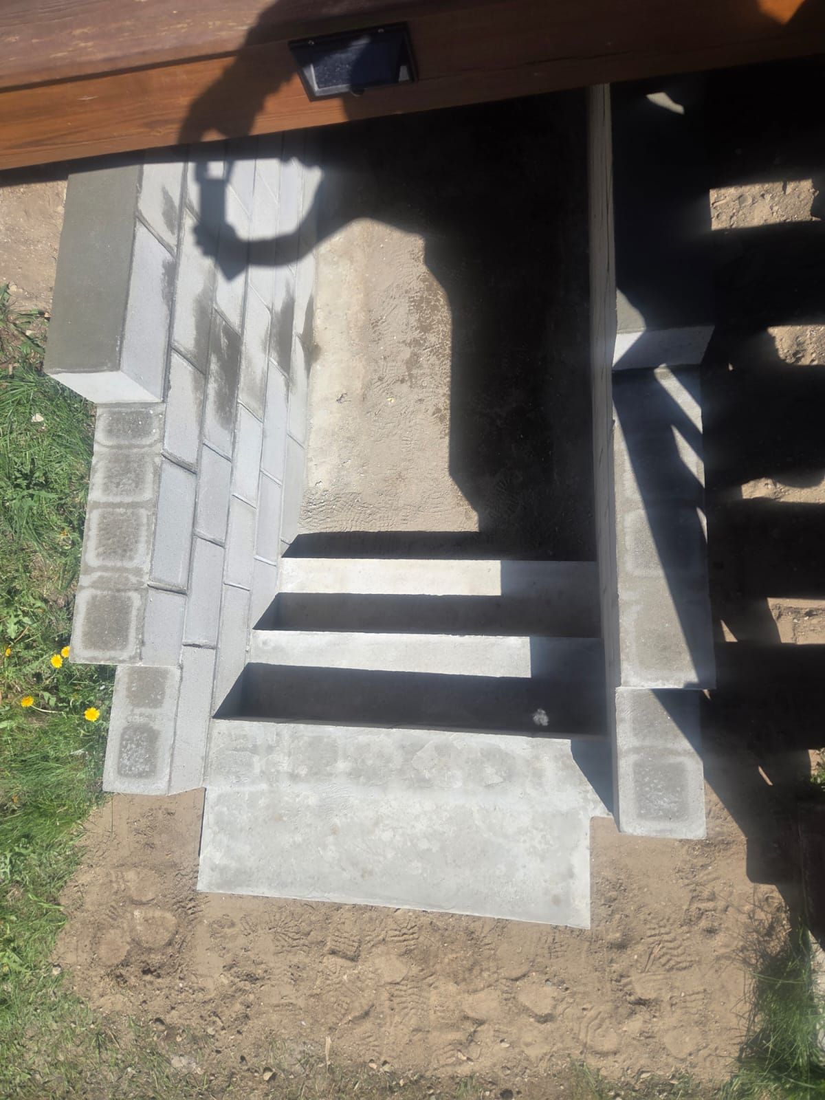 Concrete steps and platform under a deck, with cinder block side walls and dirt below.