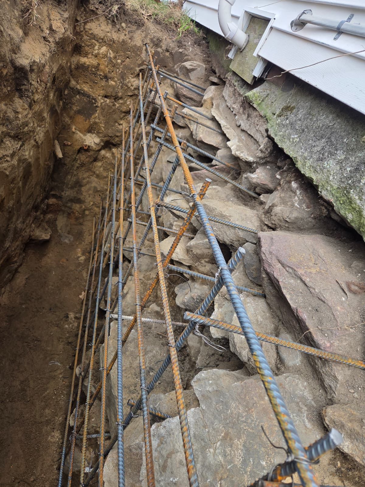 Exposed rebar and stone retaining wall beside a house during excavation work