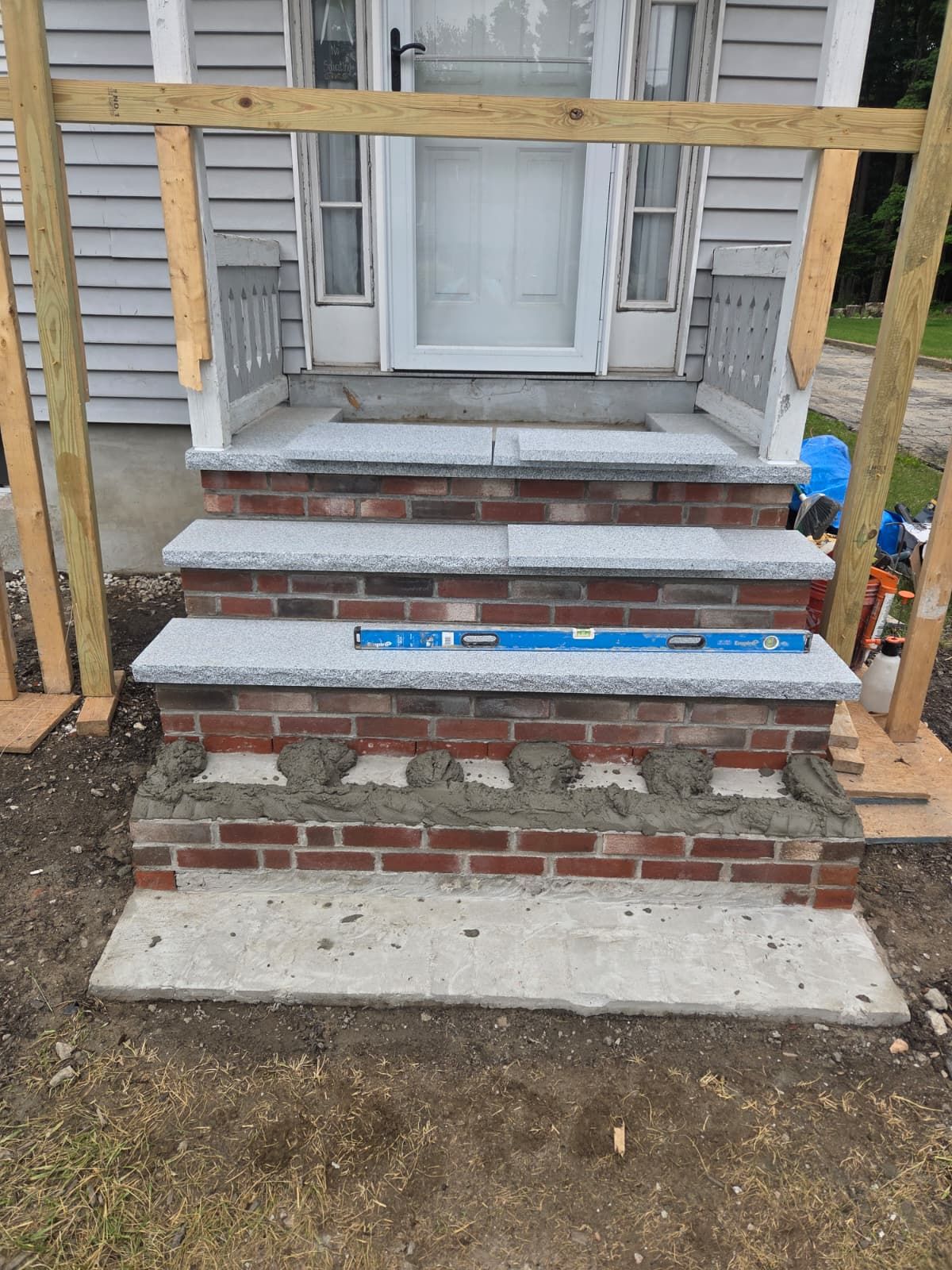Brick front steps and porch under construction with wooden framing and a white door.