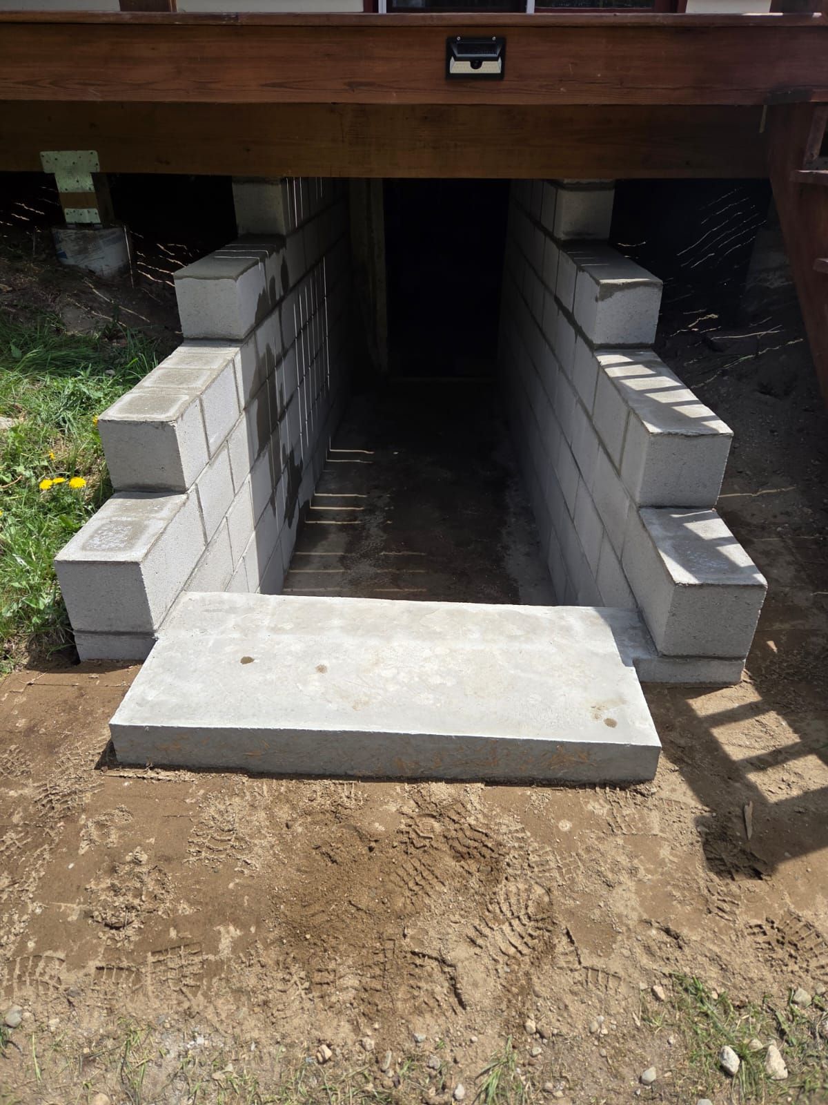 Brick-lined crawlspace entrance with concrete steps under a wooden deck