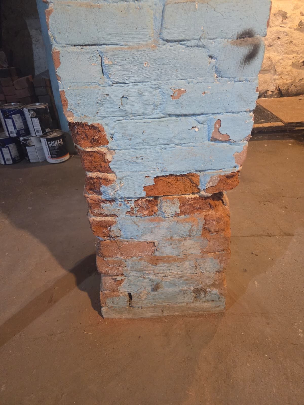 Close-up of a chipped blue-painted brick pillar with exposed red bricks in a workshop or basement.