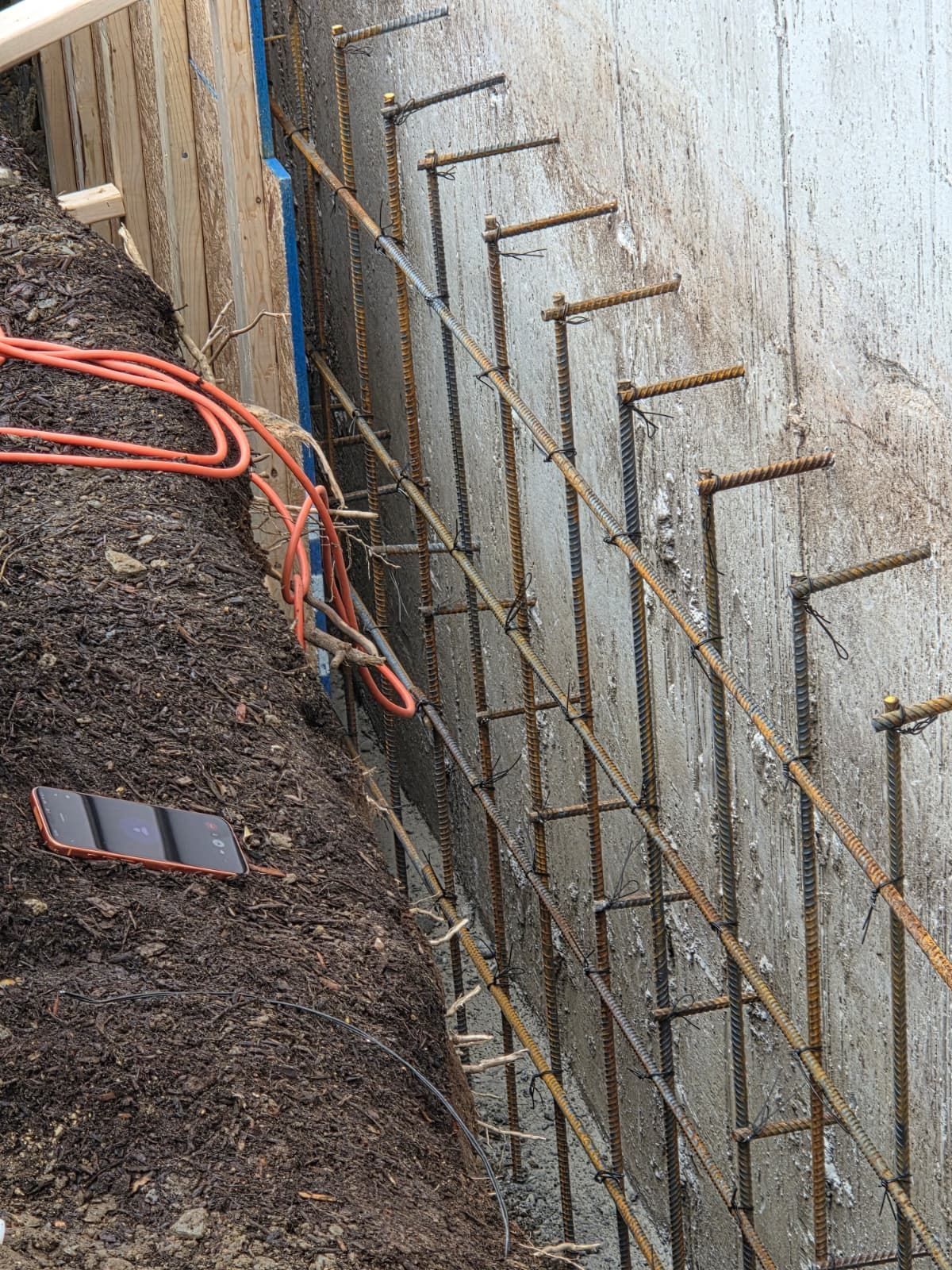 Construction site with rebar framework beside a concrete wall and orange cables on dirt ground