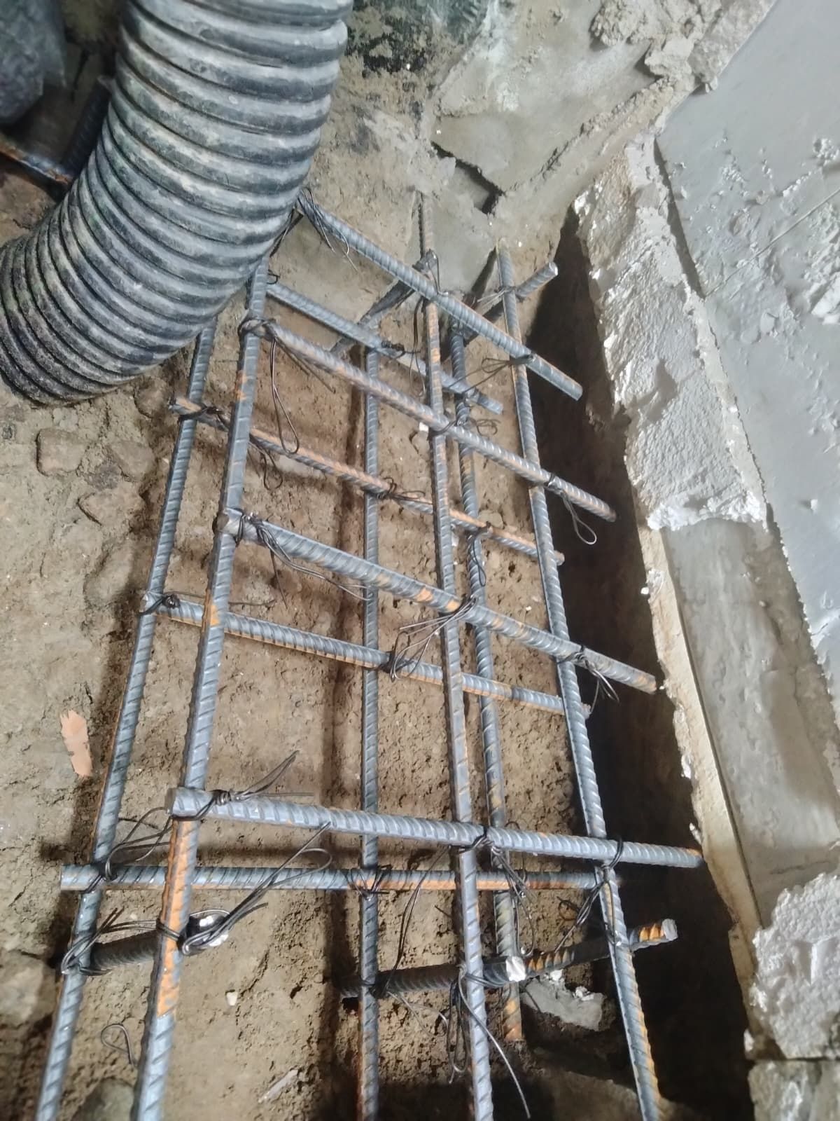 Rusty rebar grid in a trench beside a corrugated hose, preparing concrete reinforcement