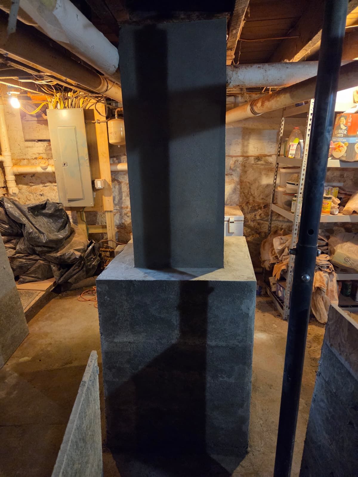 Basement with a metal duct rising from a dark furnace or boiler in a cluttered industrial space