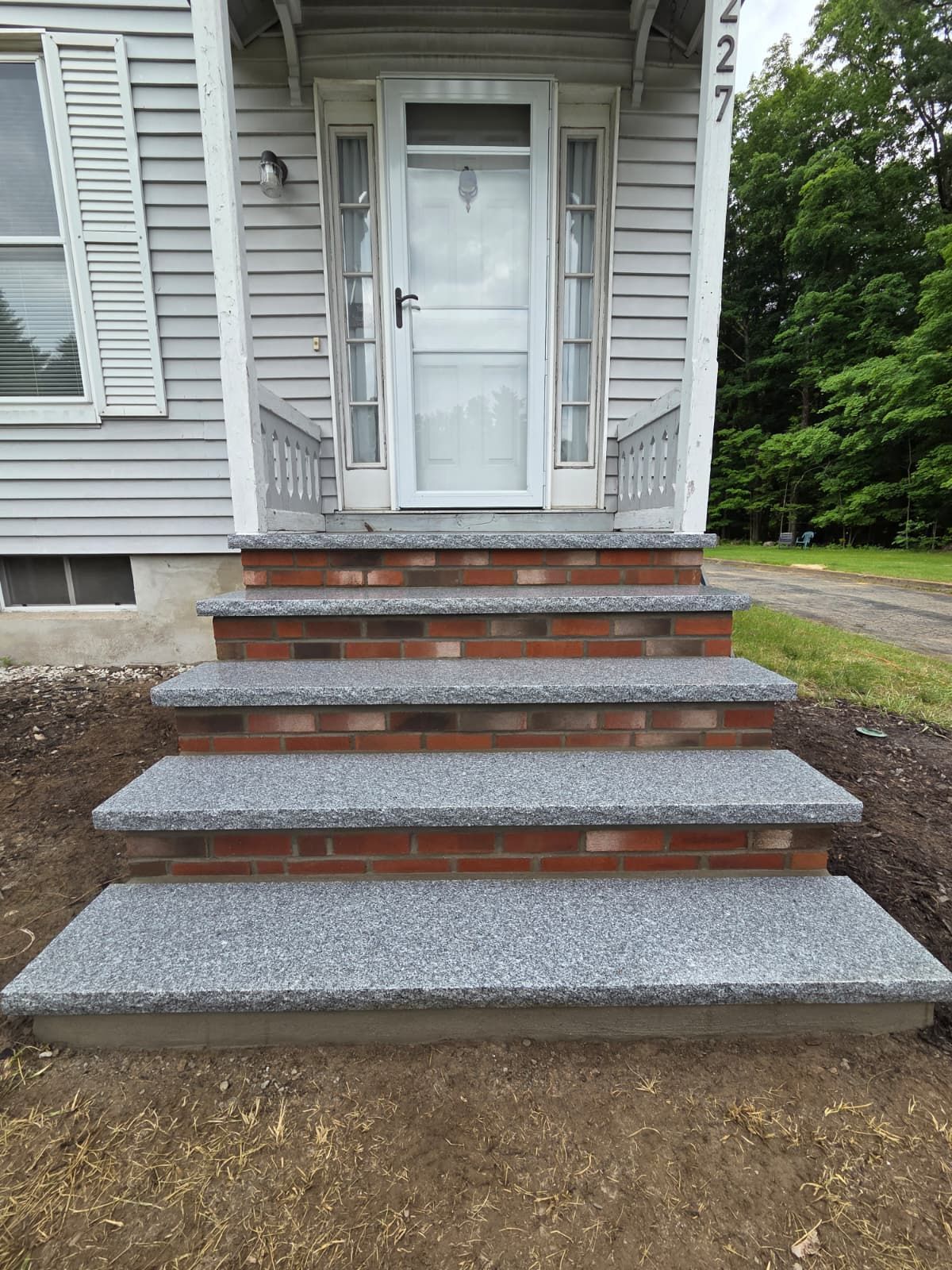 Front steps with brick risers and gray concrete treads leading to a white house door