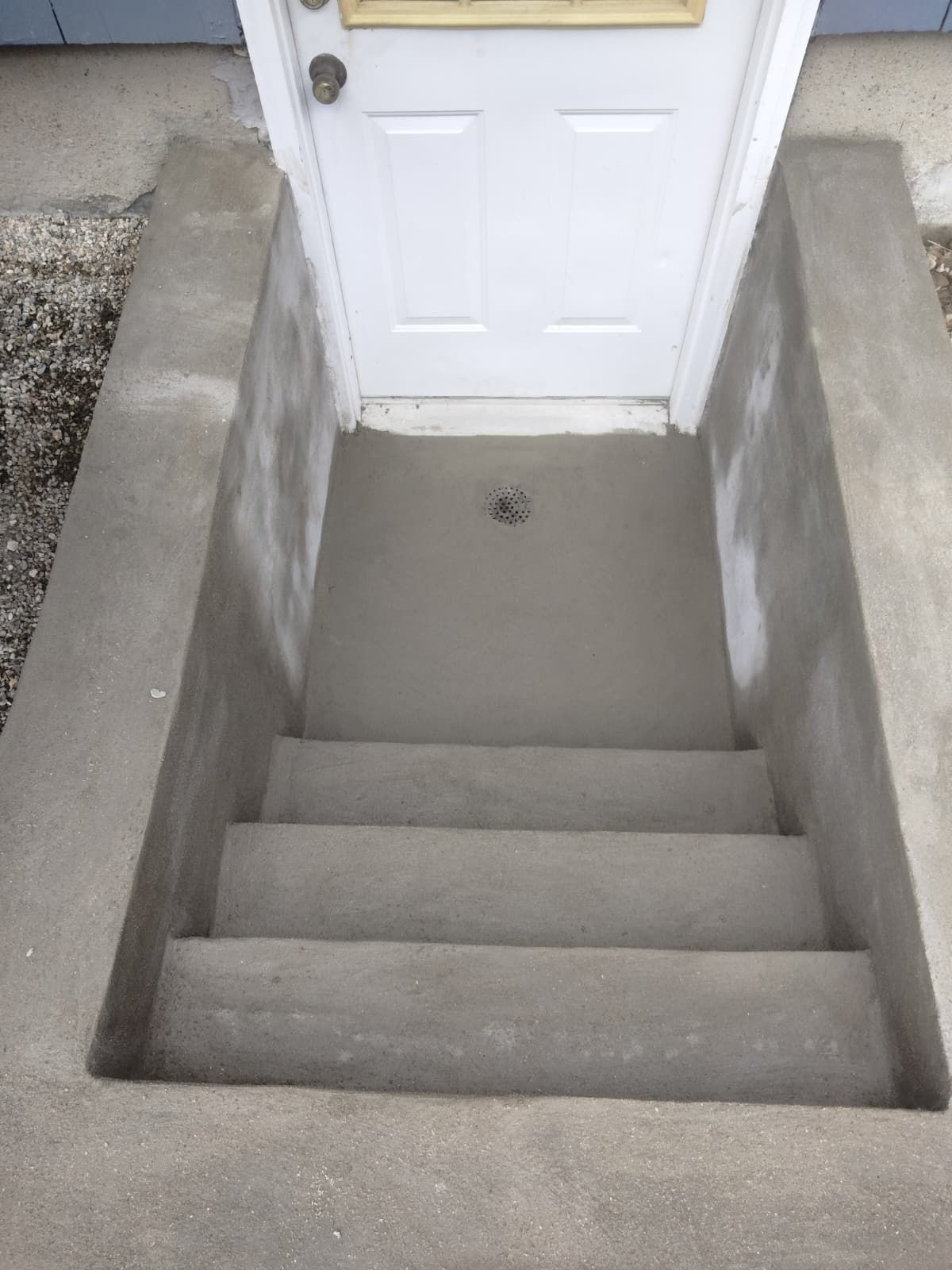 Concrete stairwell leading up to a white door with gray walls and a small landing