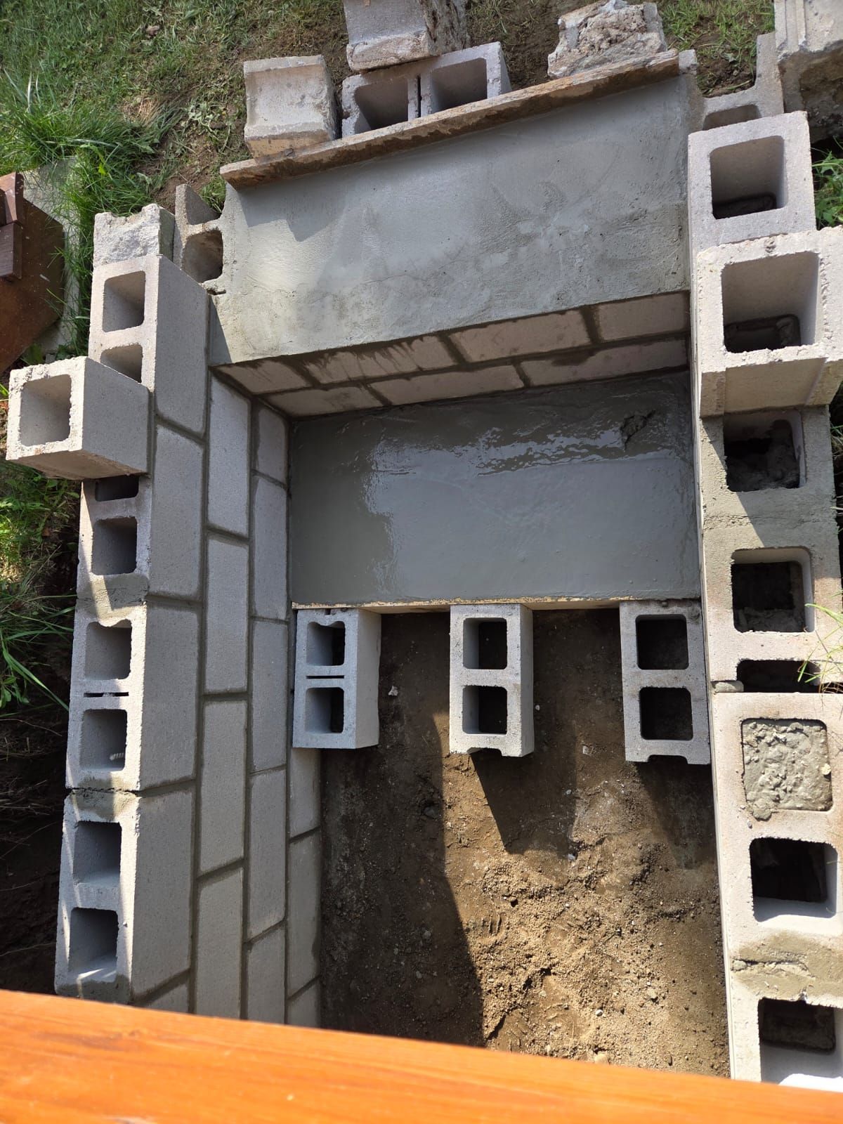 Partially built cinder block structure with gray concrete and exposed dirt foundation