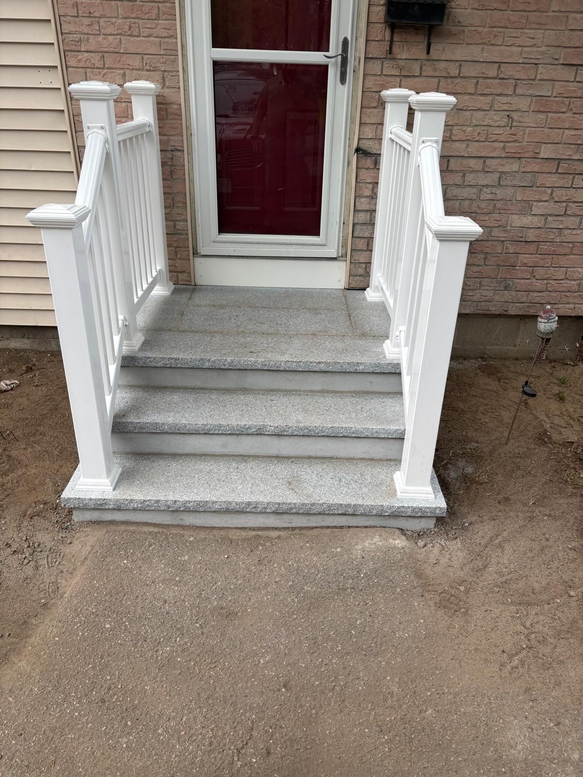 Front steps with white railings leading to a red front door and tan siding.