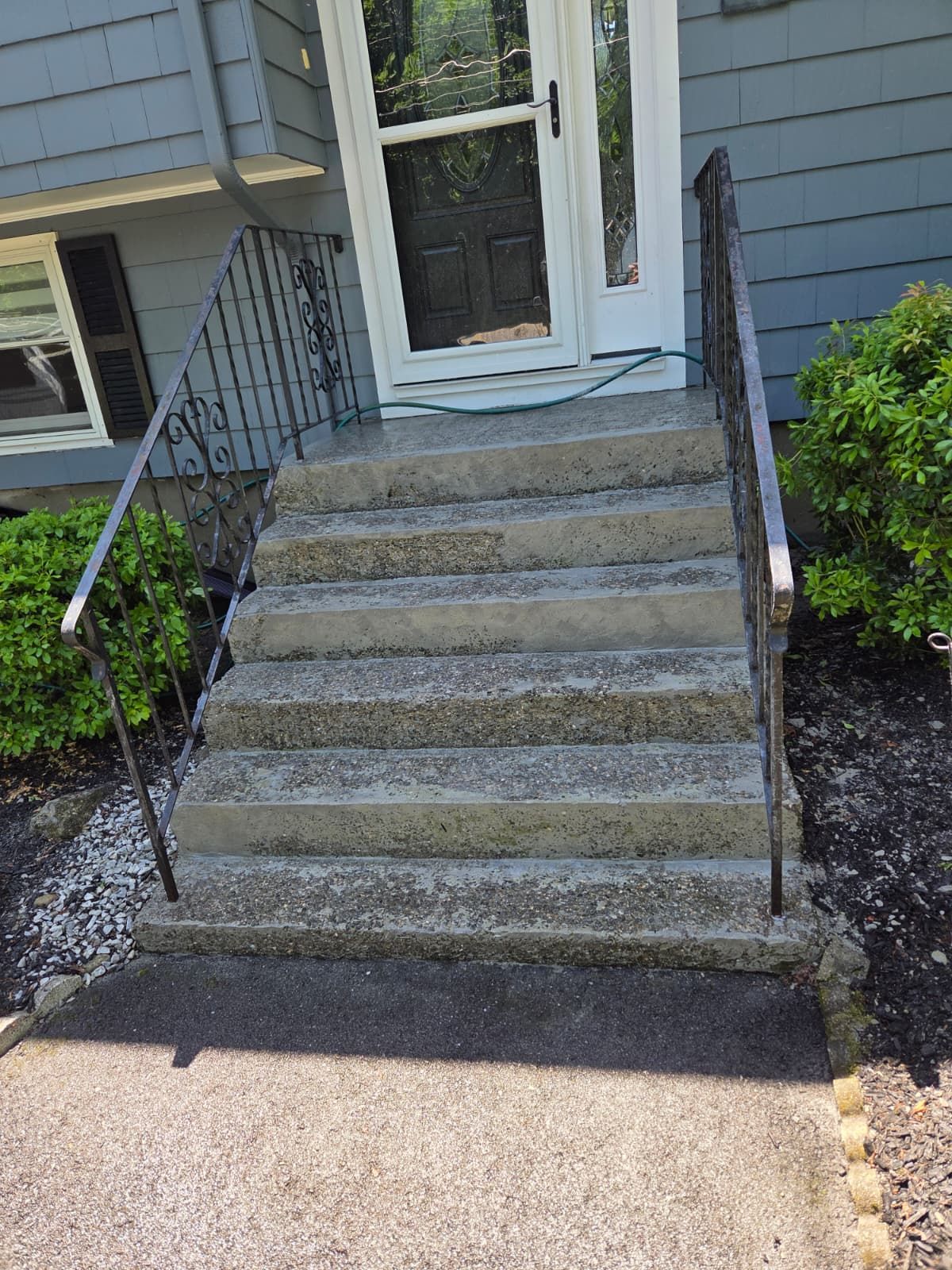 Concrete front steps with black railings leading to a white front door of a gray house.