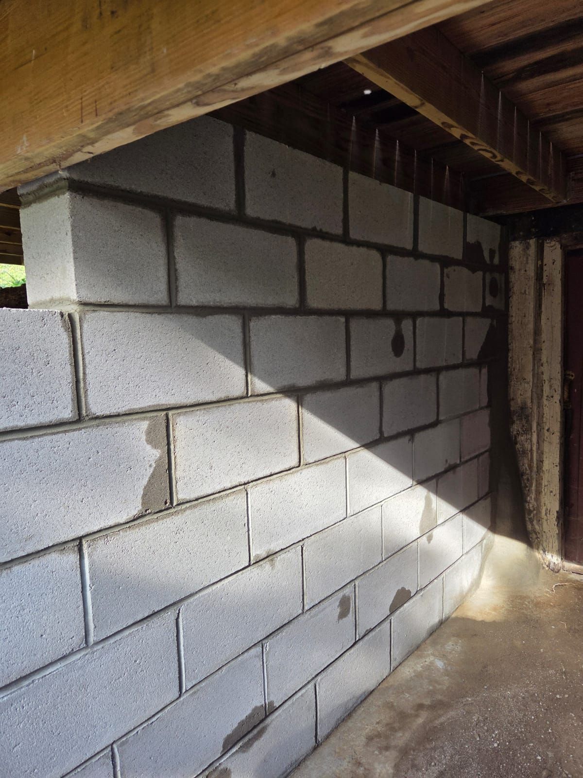 Gray cinderblock wall under a wooden deck, with sunlight casting a diagonal shadow on the concrete floor.