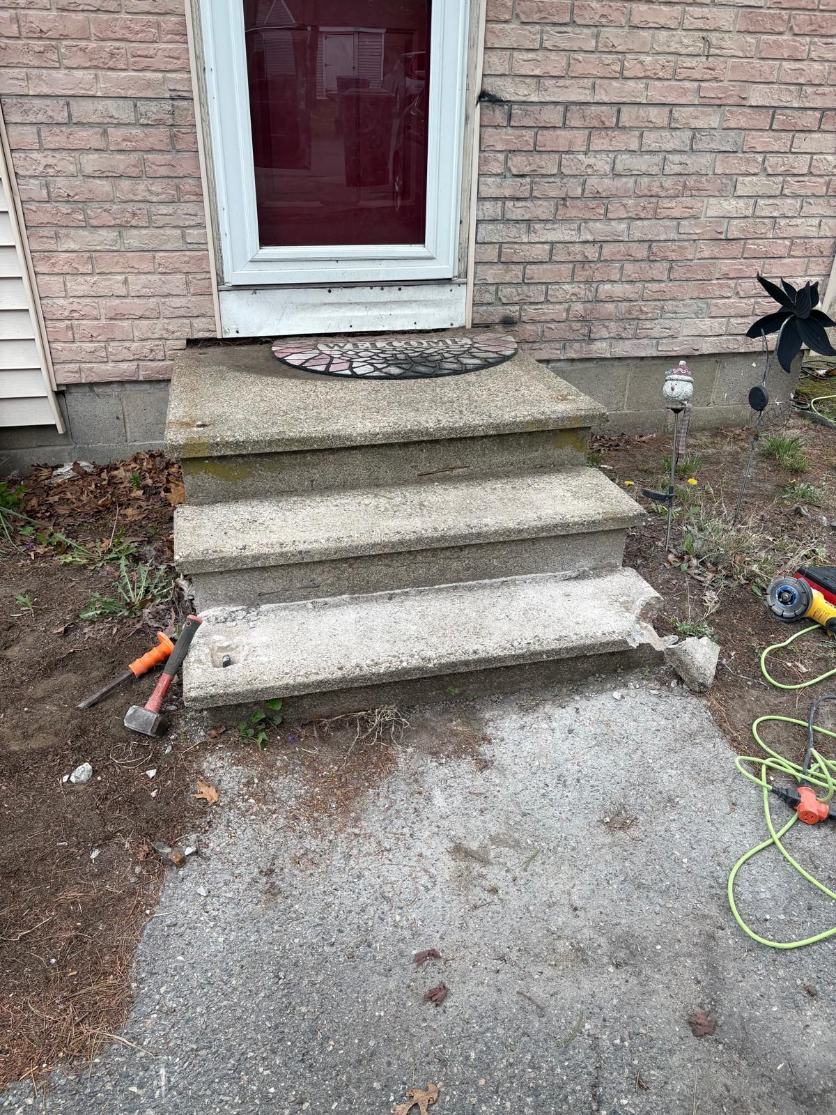 Concrete front steps and porch against a brick wall, with scattered tools and cords on the ground.