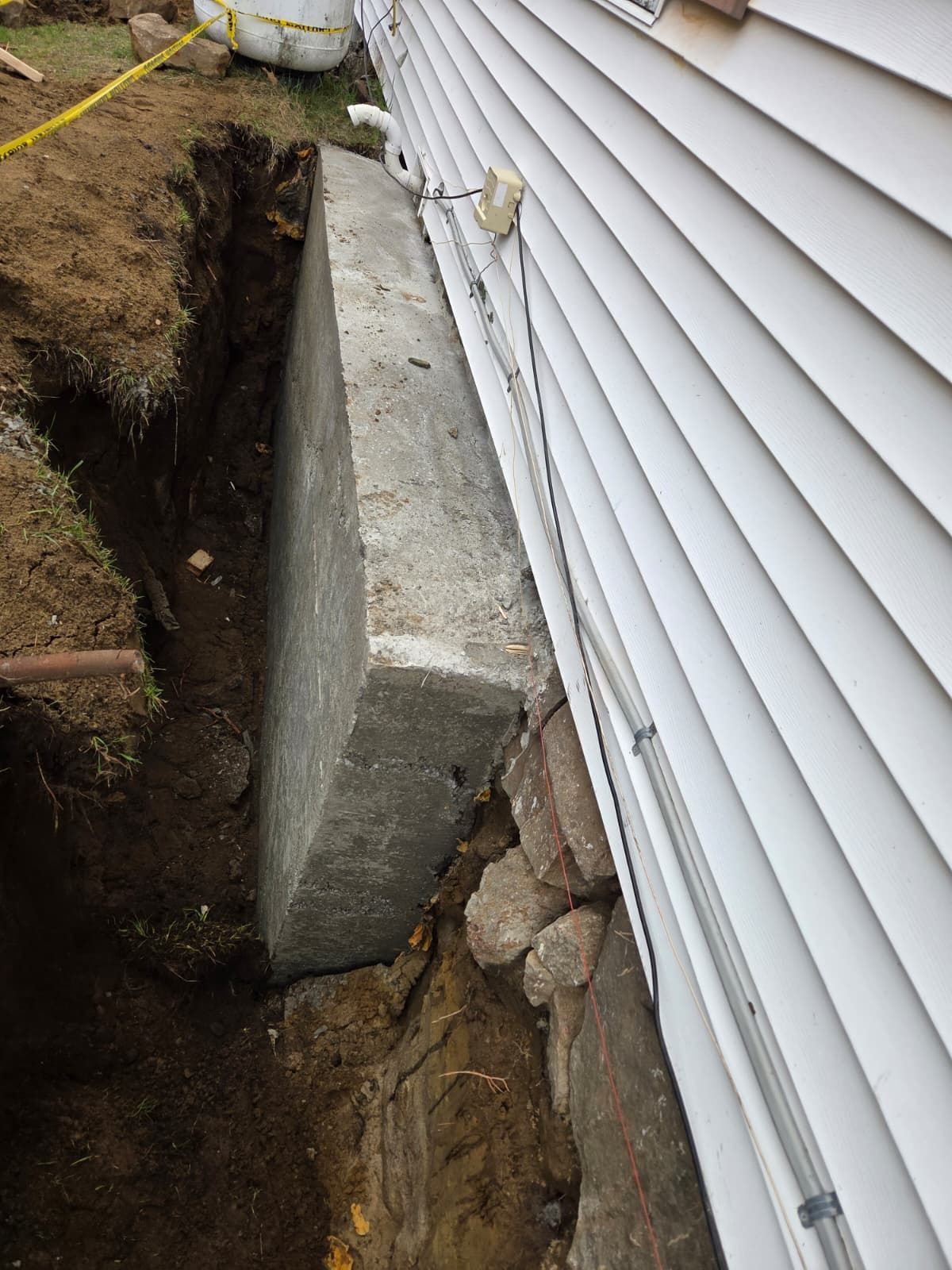 Concrete foundation beside house siding with an excavated trench and exposed soil and rocks
